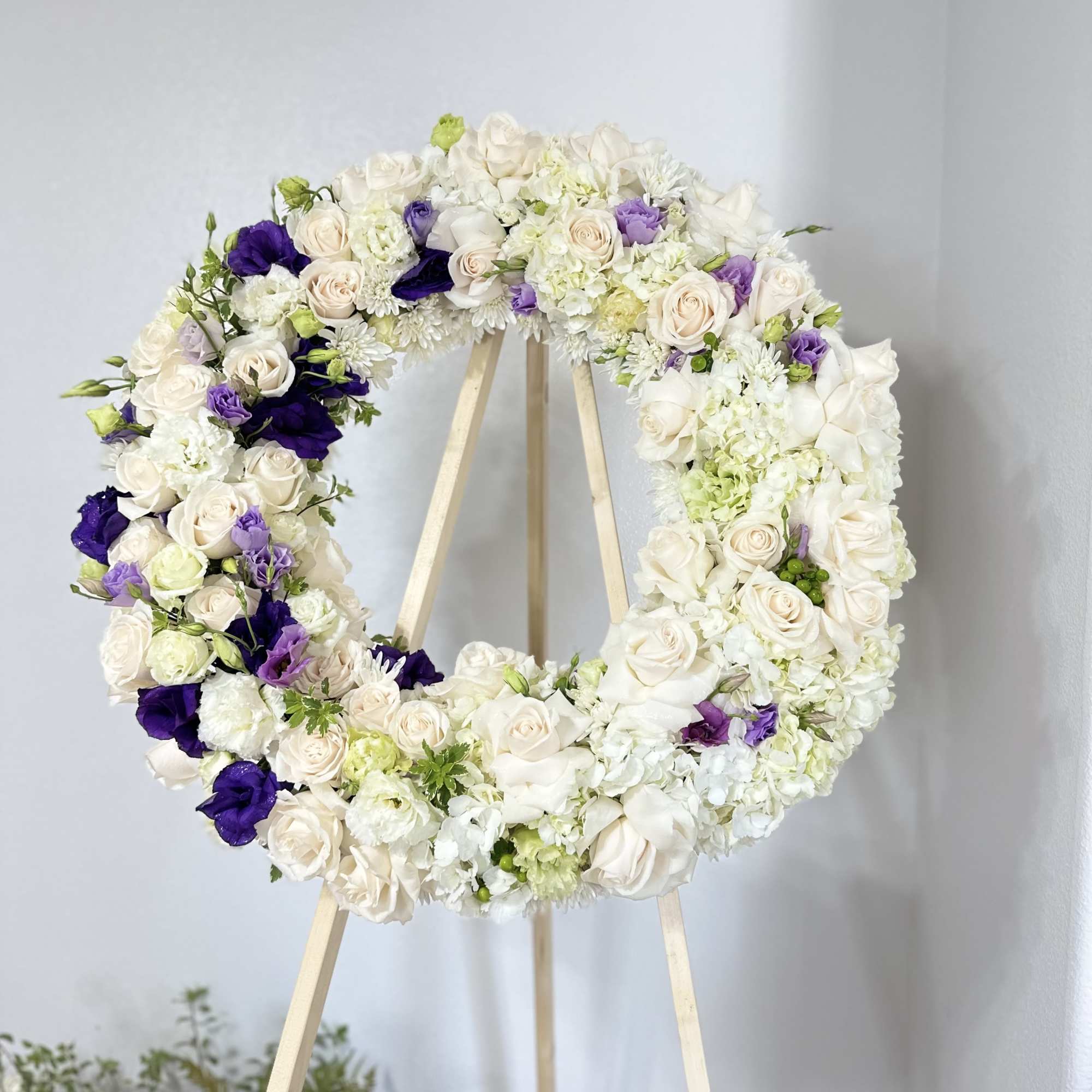 This sympathy wreath features ivory roses, hydrangeas, and chrysanthemums, accented with delicate