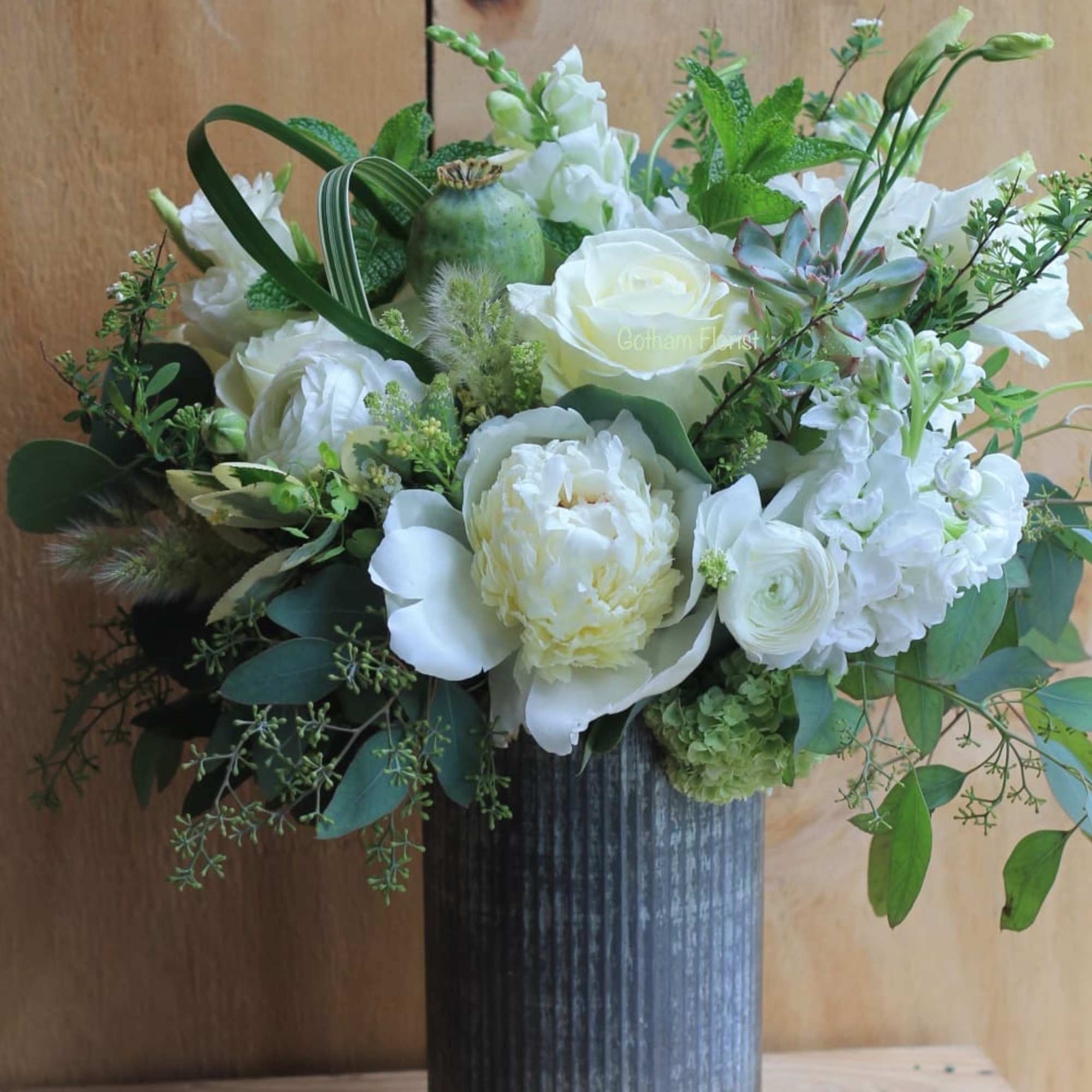 Tin vase filled with white seasonal flowers, lush greenery, succulents and herbs.