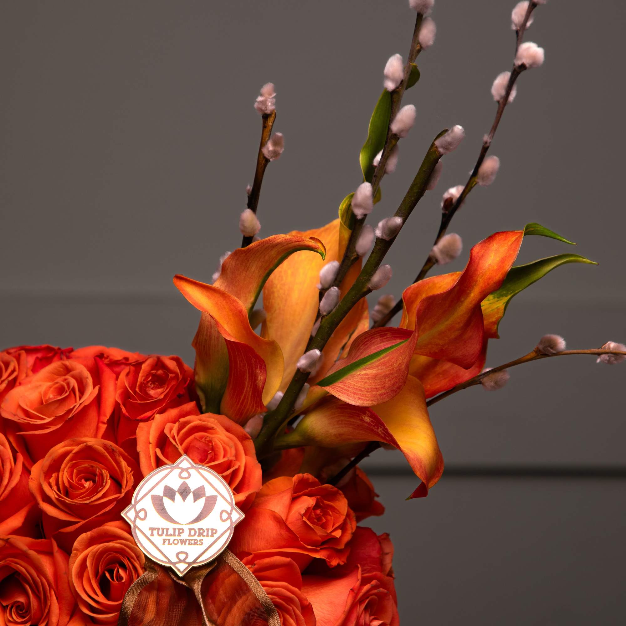 This striking arrangement features vibrant orange roses and calla lilies styled into