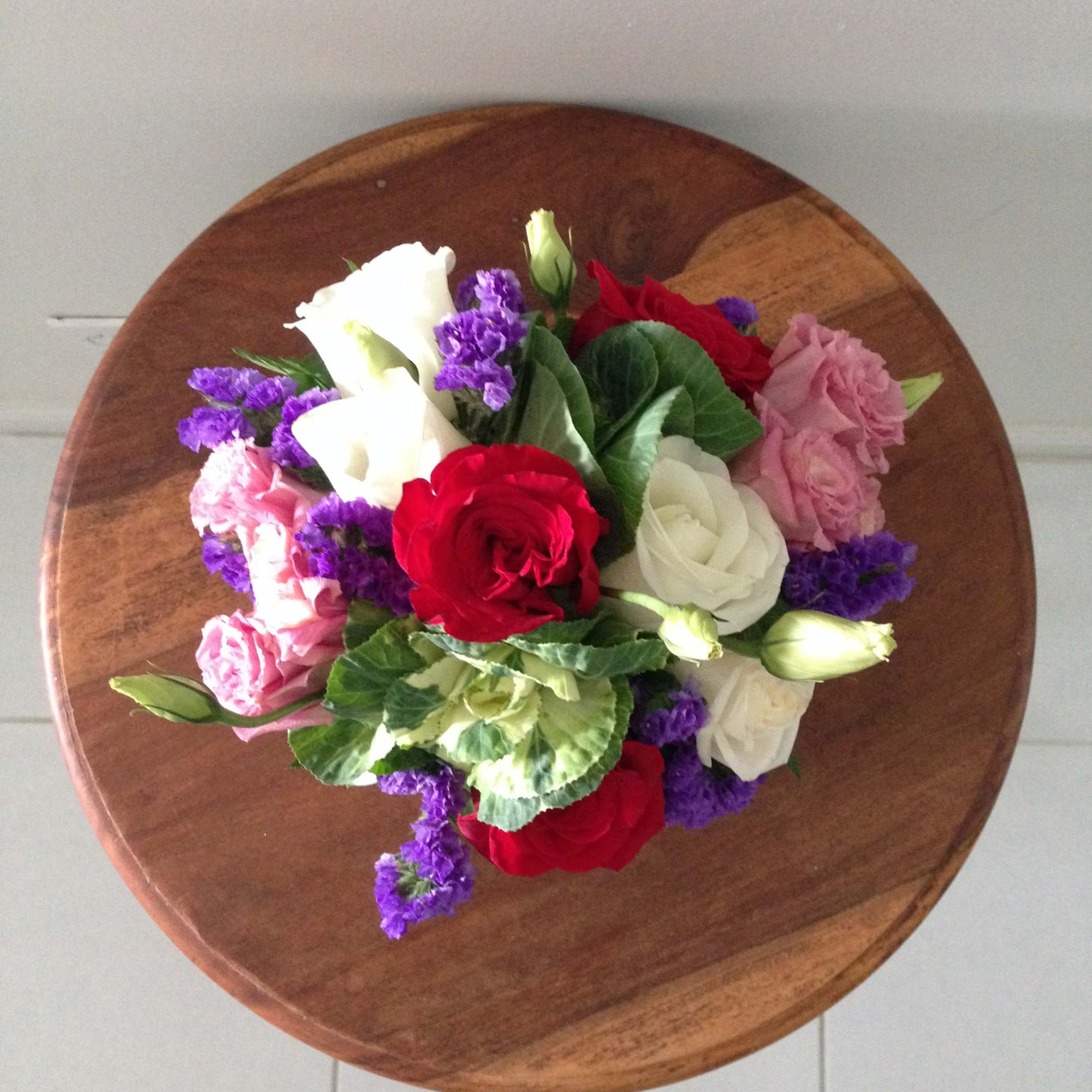 Multicolored surprise with purple statice, white kale and a variety of roses.