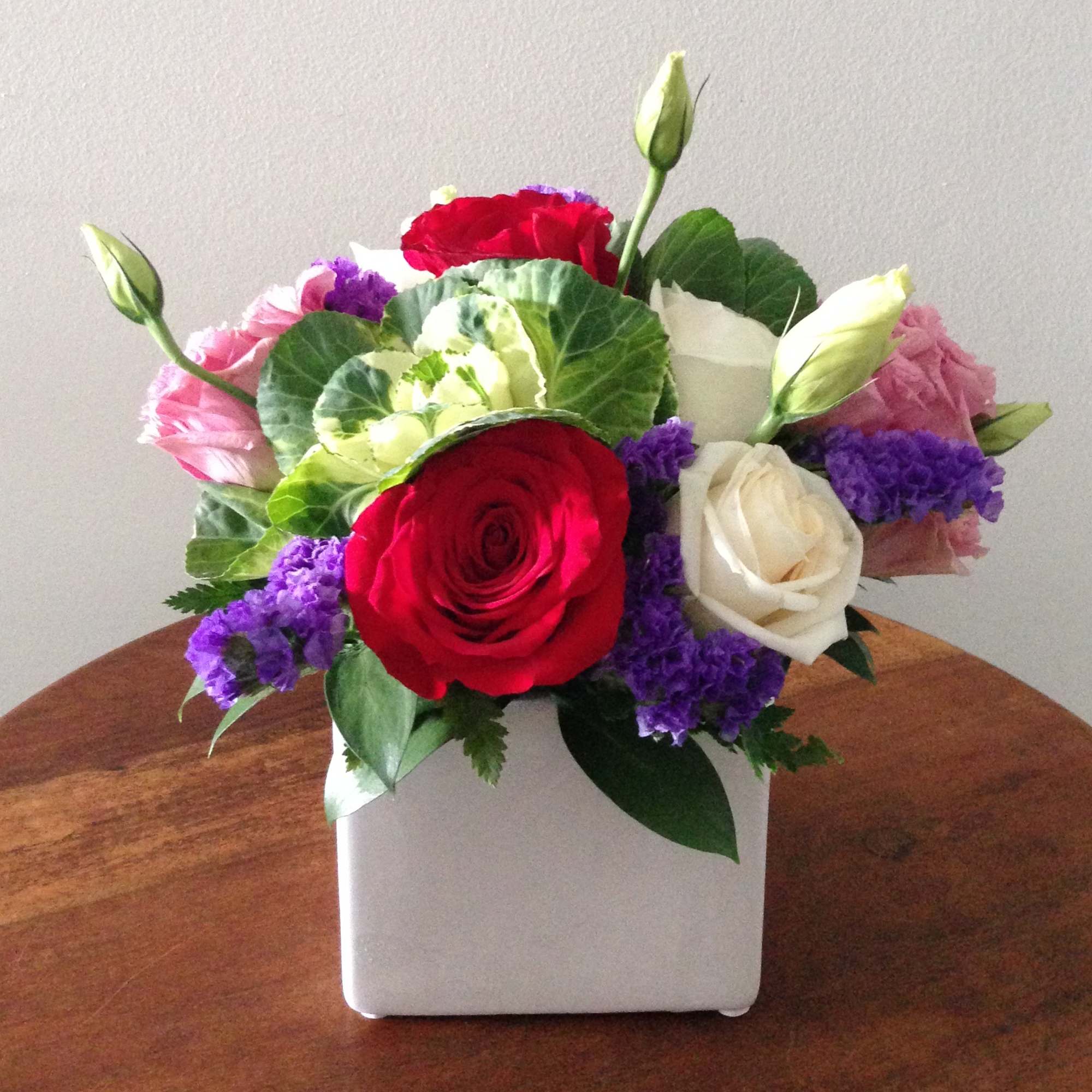 Multicolored surprise with purple statice, white kale and a variety of roses.