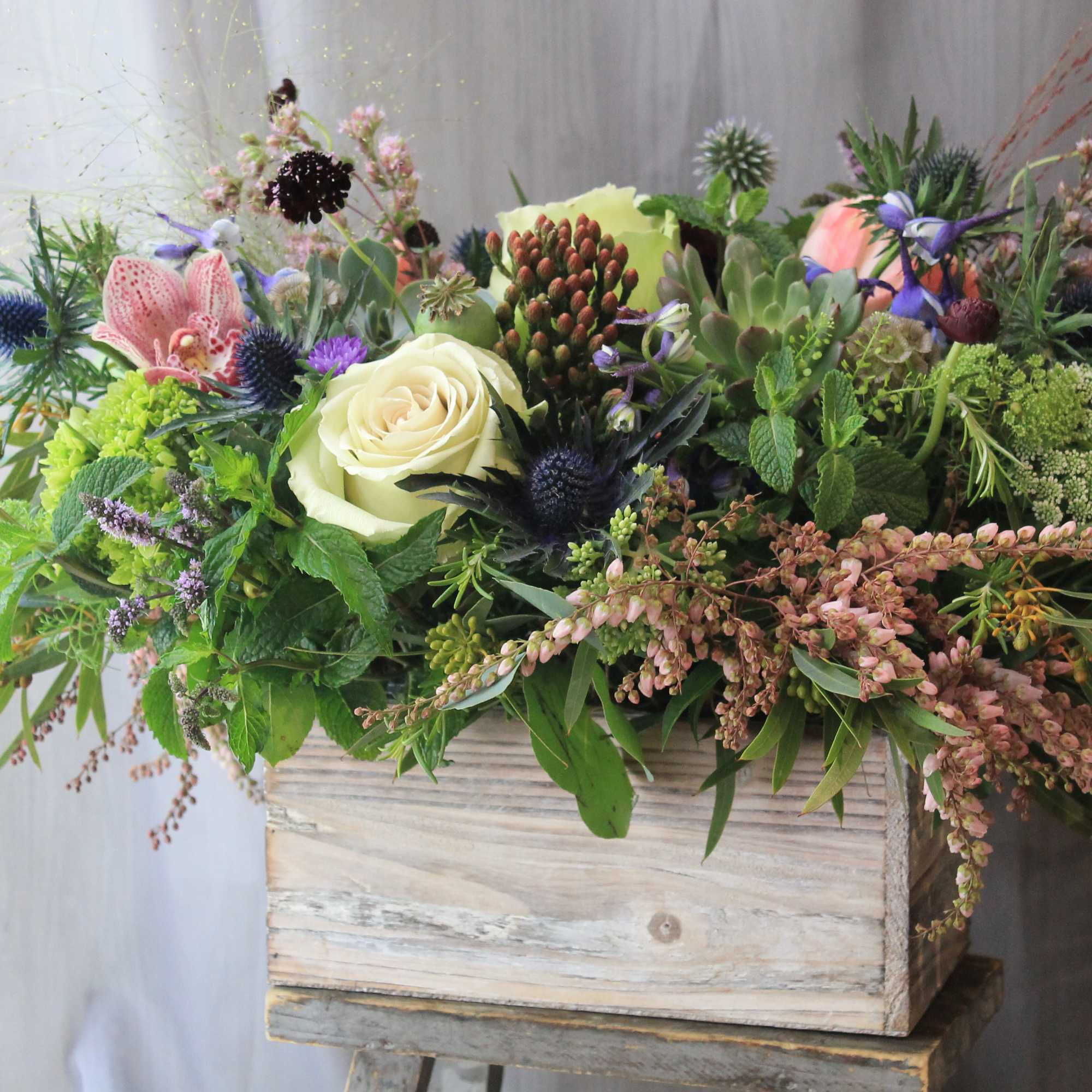 Natural wood box filled with blue and green flowers and a succulent