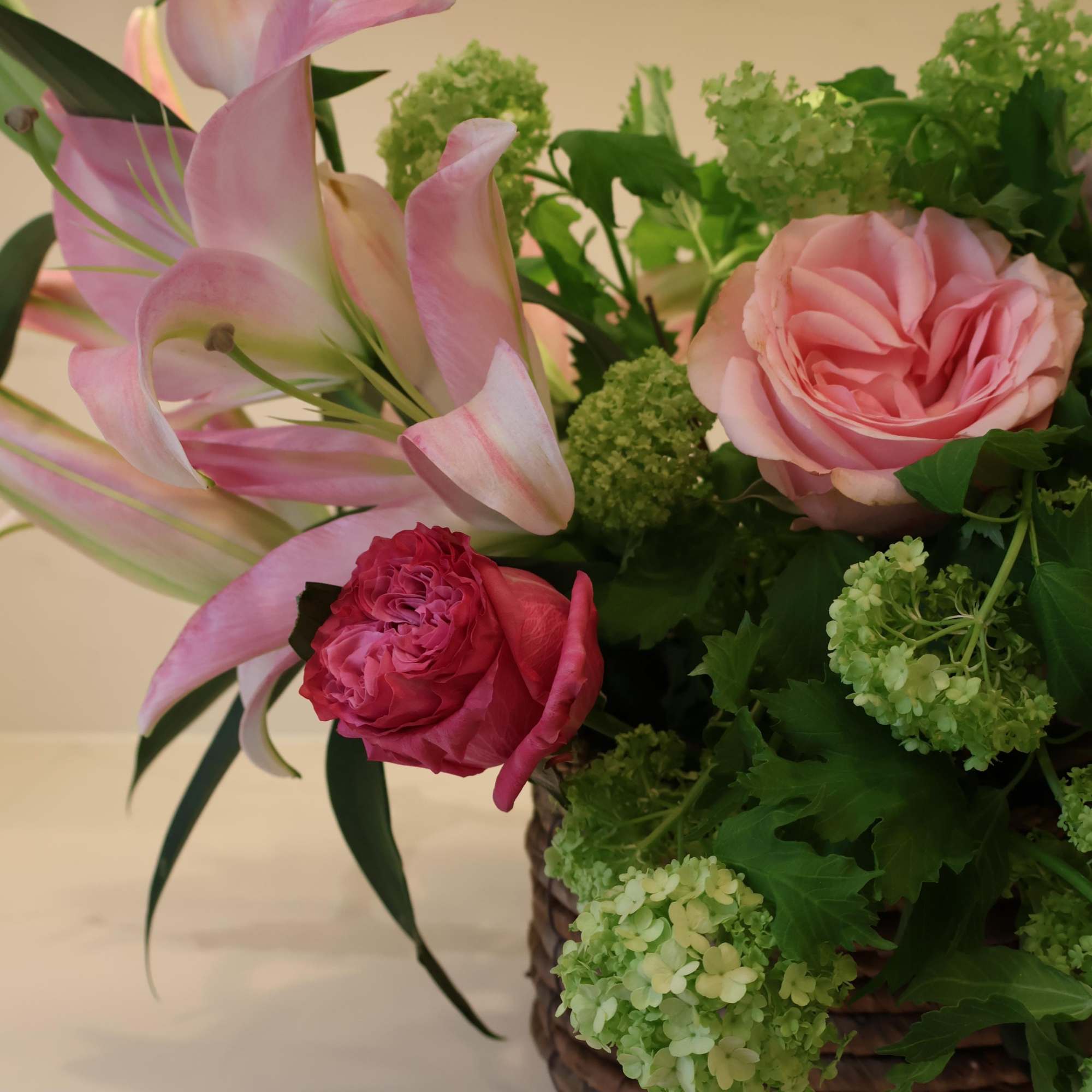 A charming basket of blush roses, pink lilies, lavender stock, and fresh