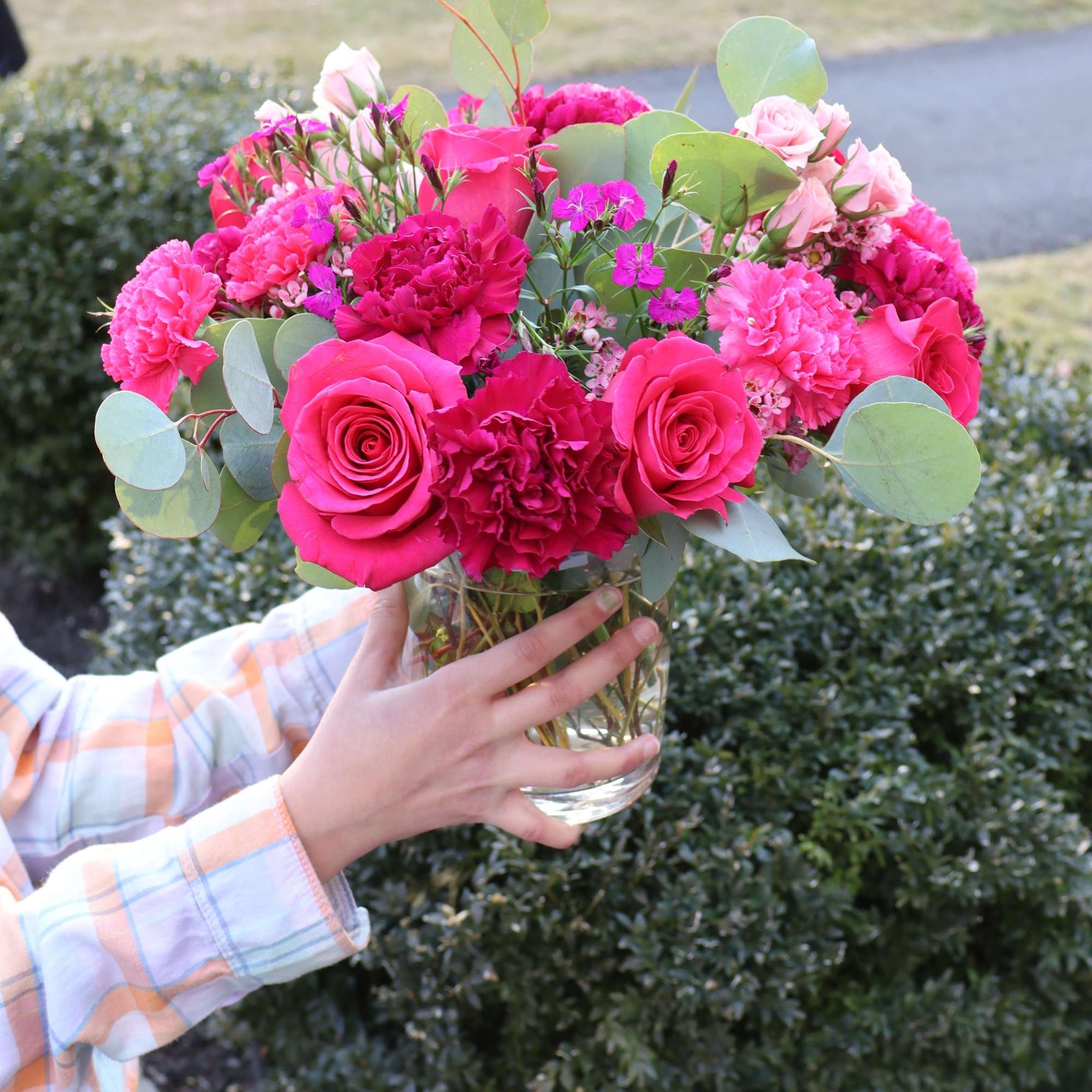 A lush and romantic floral arrangement featuring deep magenta roses, vibrant carnations