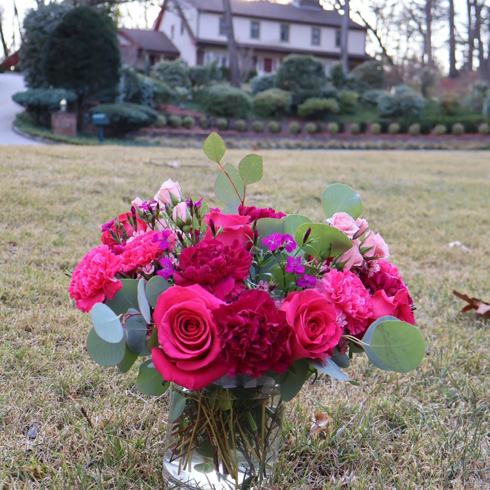 A lush and romantic floral arrangement featuring deep magenta roses, vibrant carnations
