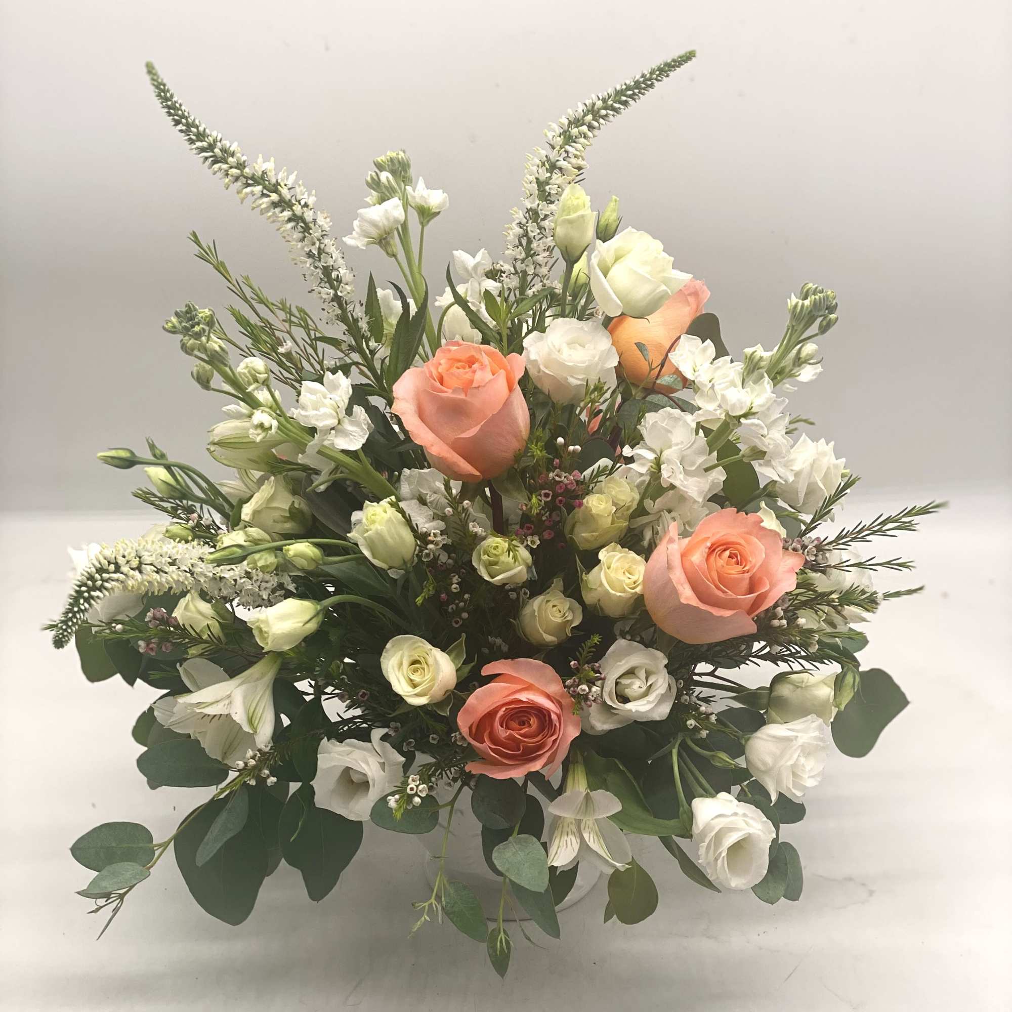This arrangement features soft coral roses as the focal point, complimented by