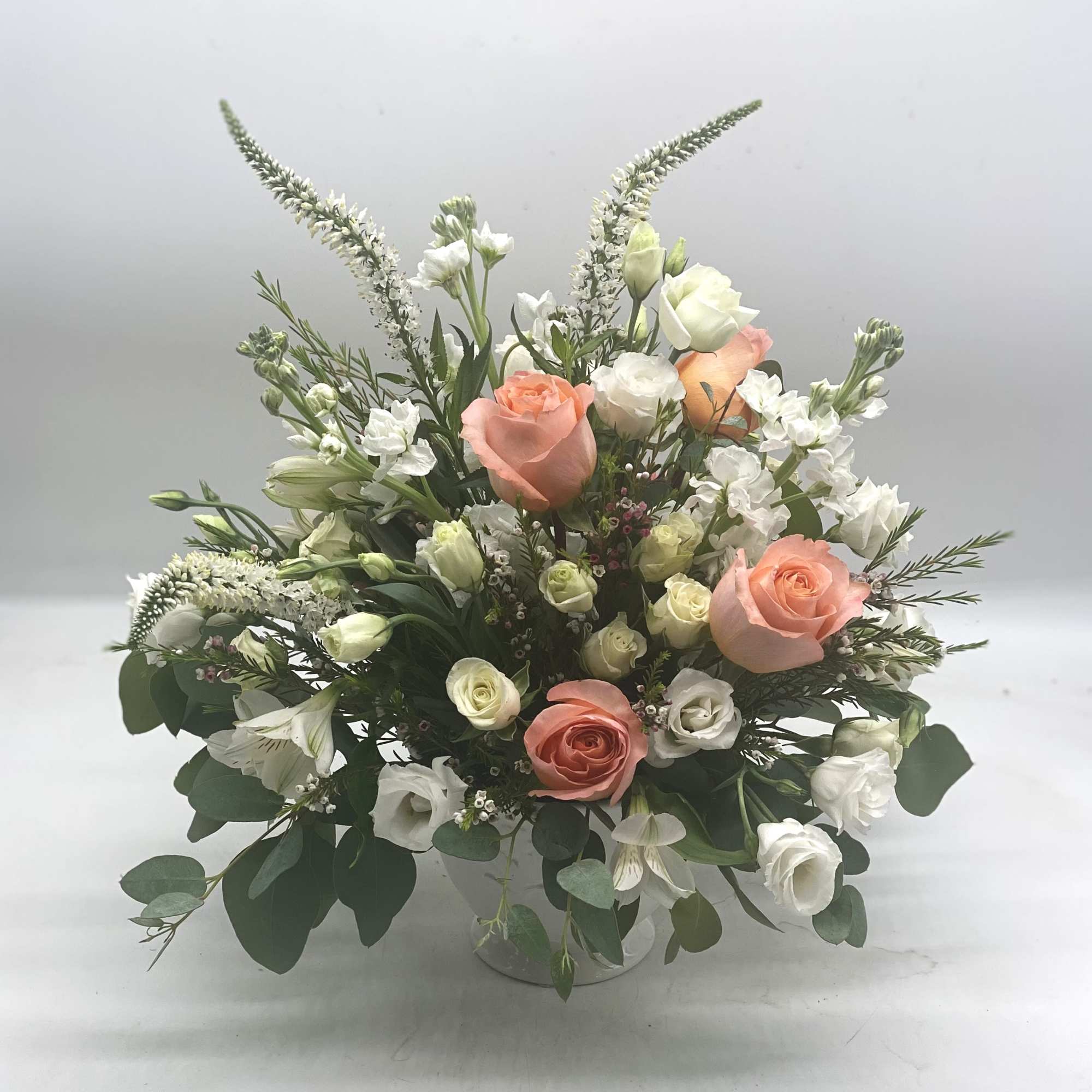 This arrangement features soft coral roses as the focal point, complimented by