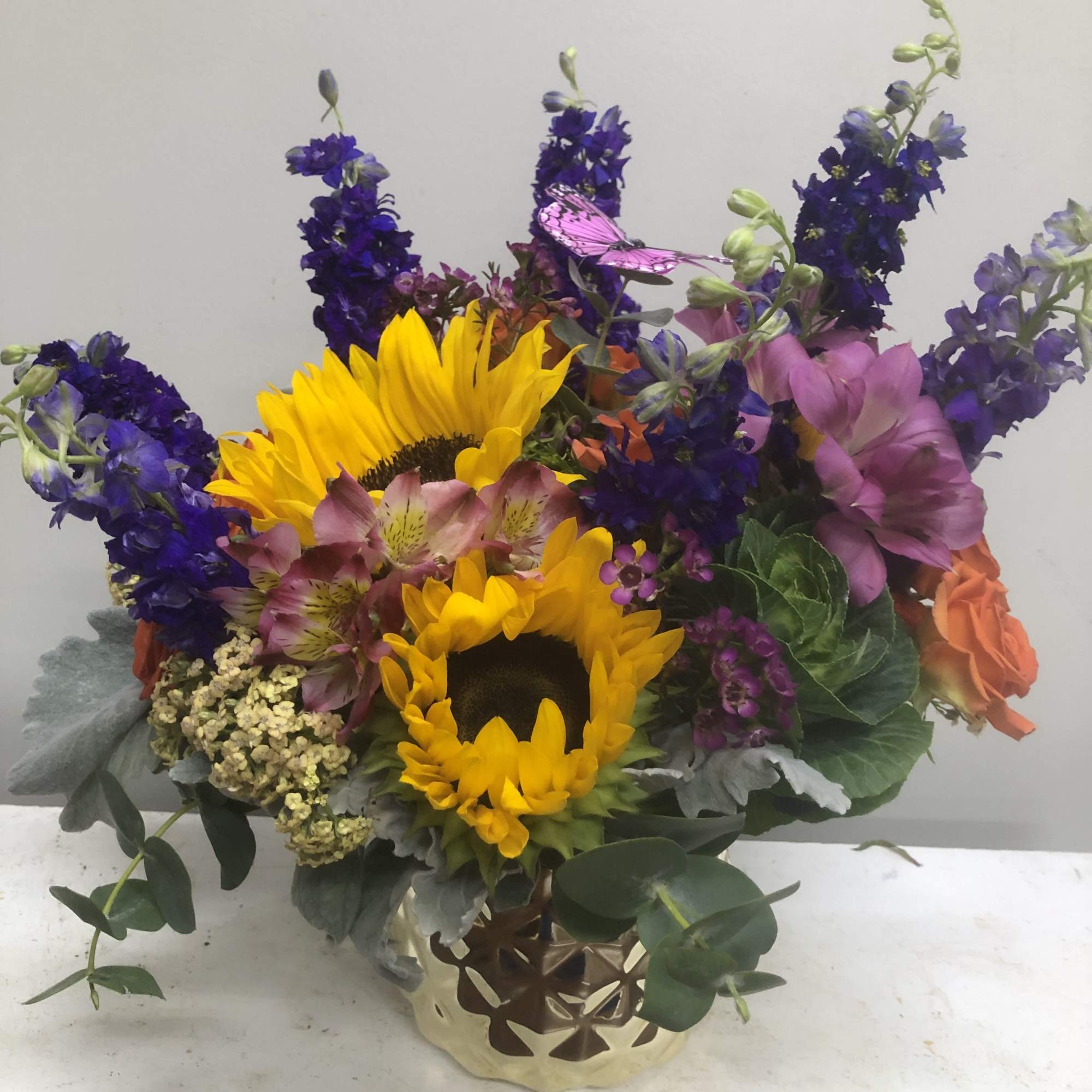 Sunflowers surrounded by orange roses, alstroemeria, and purple larkspur.