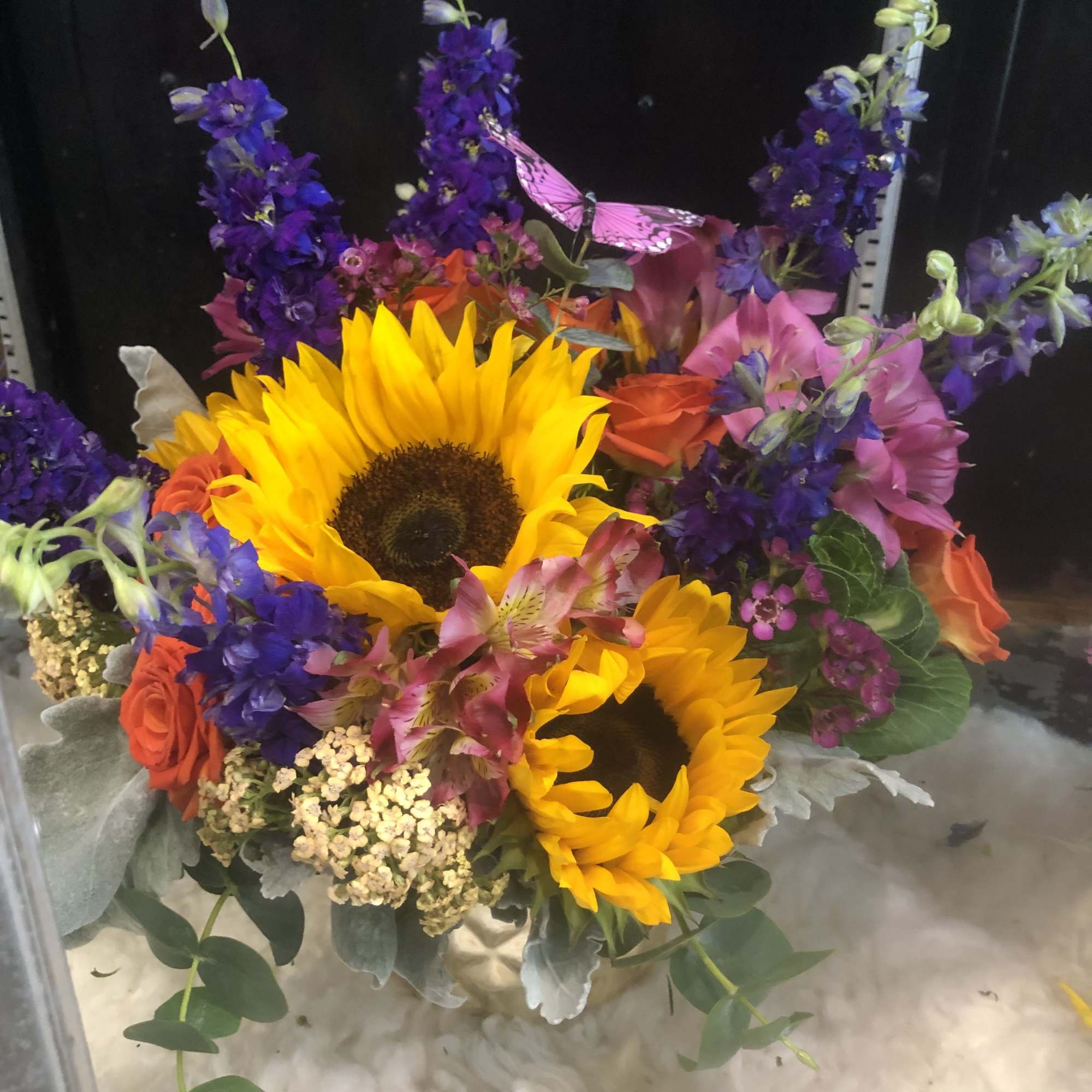 Sunflowers surrounded by orange roses, alstroemeria, and purple larkspur.