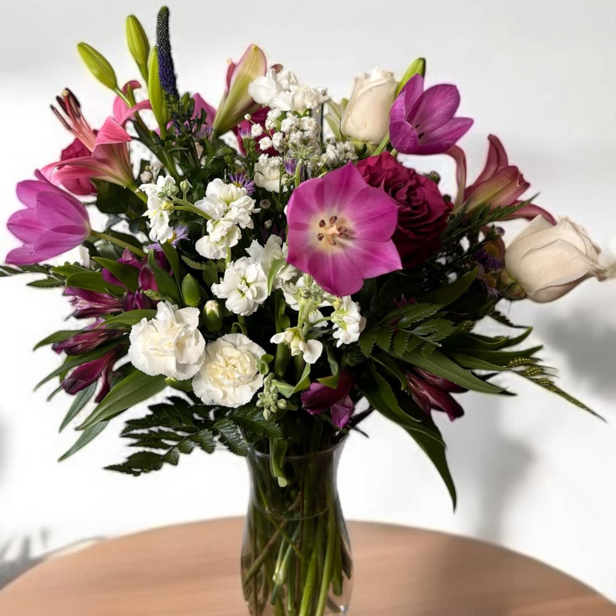This classic arrangement features purple and white seasonal flowers, hand-designed inside a