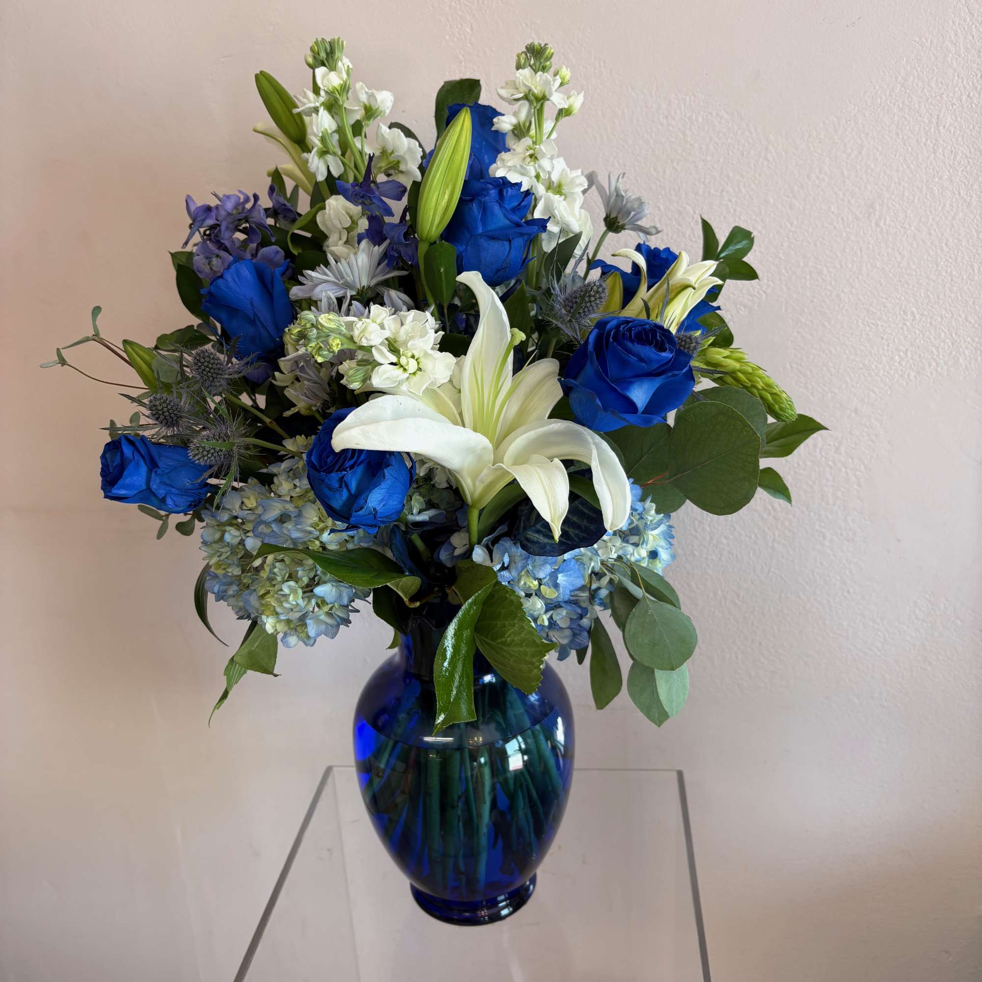 This large vase features 7 blue roses, blue hydrangeas, blue thistle, blue