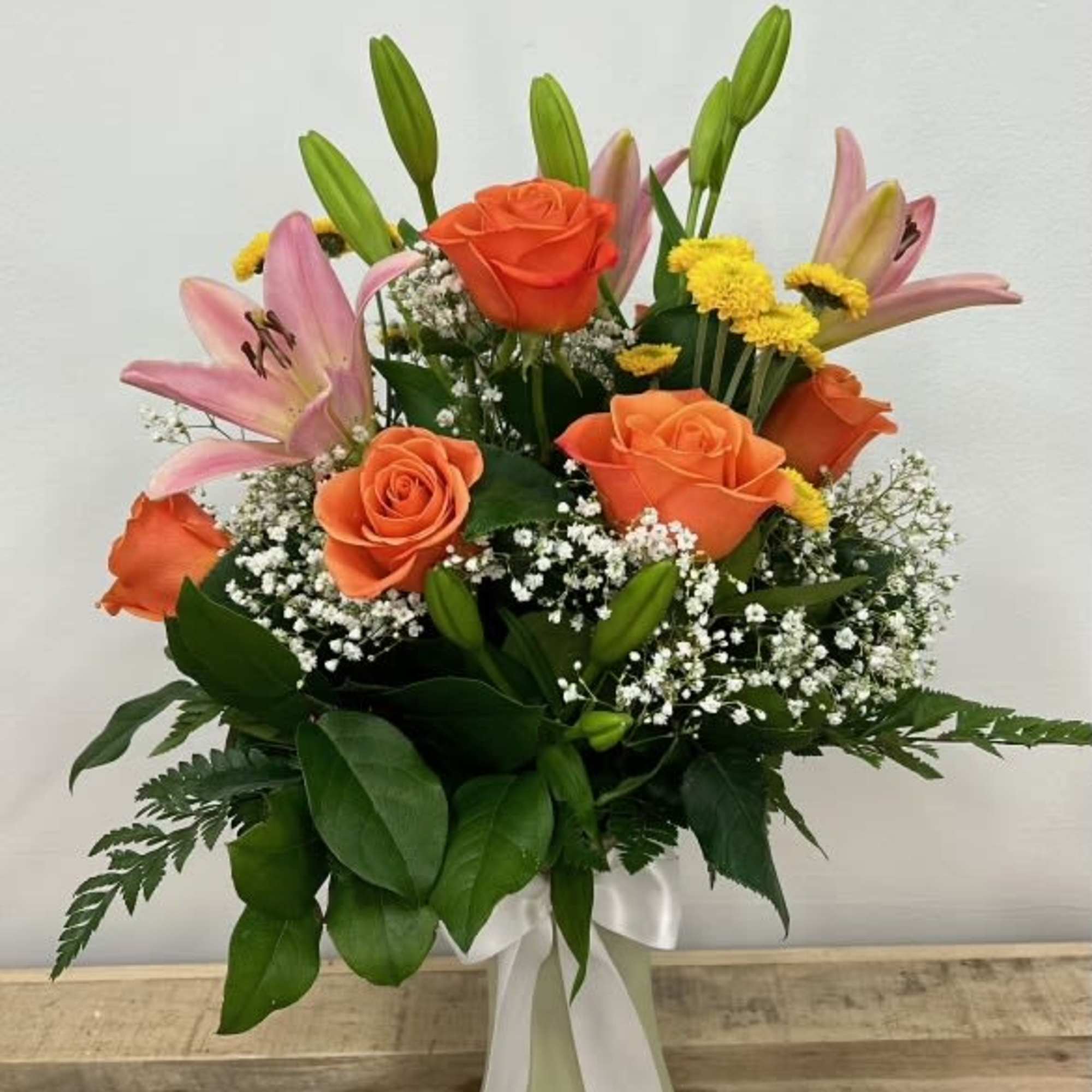 With striking pink lilies and bright orange roses, softened by delicate baby&rsquo;s