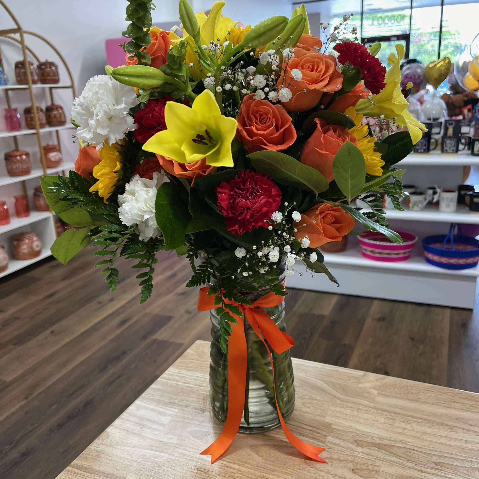 Orange roses, red, white, and yellow carnations, and bright yellow lilies are