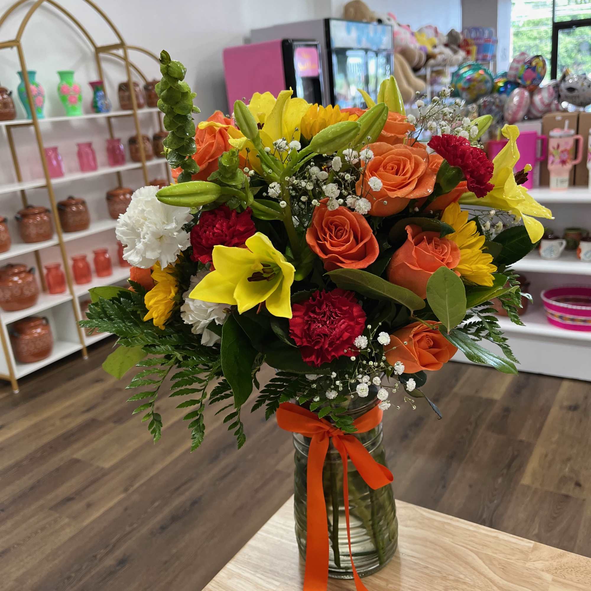 Orange roses, red, white, and yellow carnations, and bright yellow lilies are