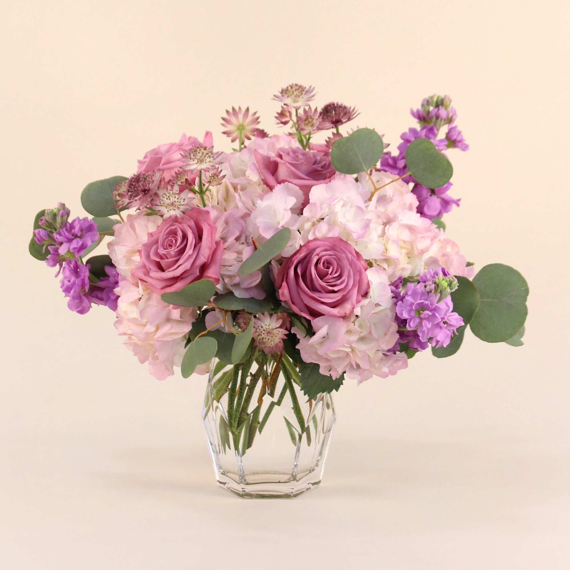 A lush arrangements of lavender and mauve flowers in a clear cylinder