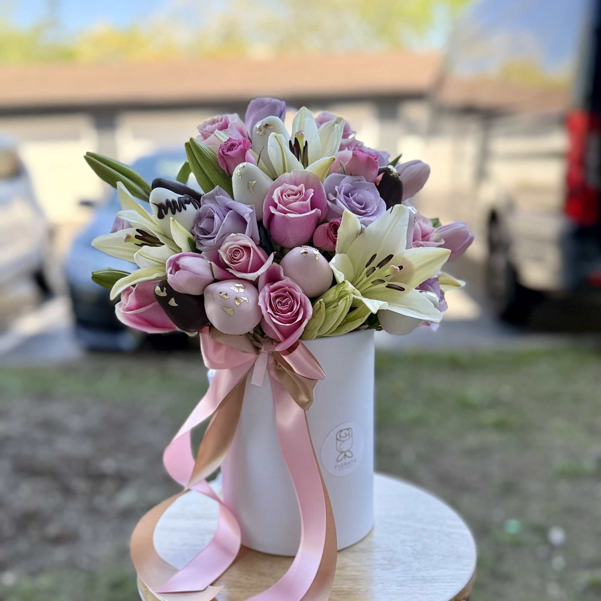 Round box combining soft lavender and pink roses with strawberries dipped in