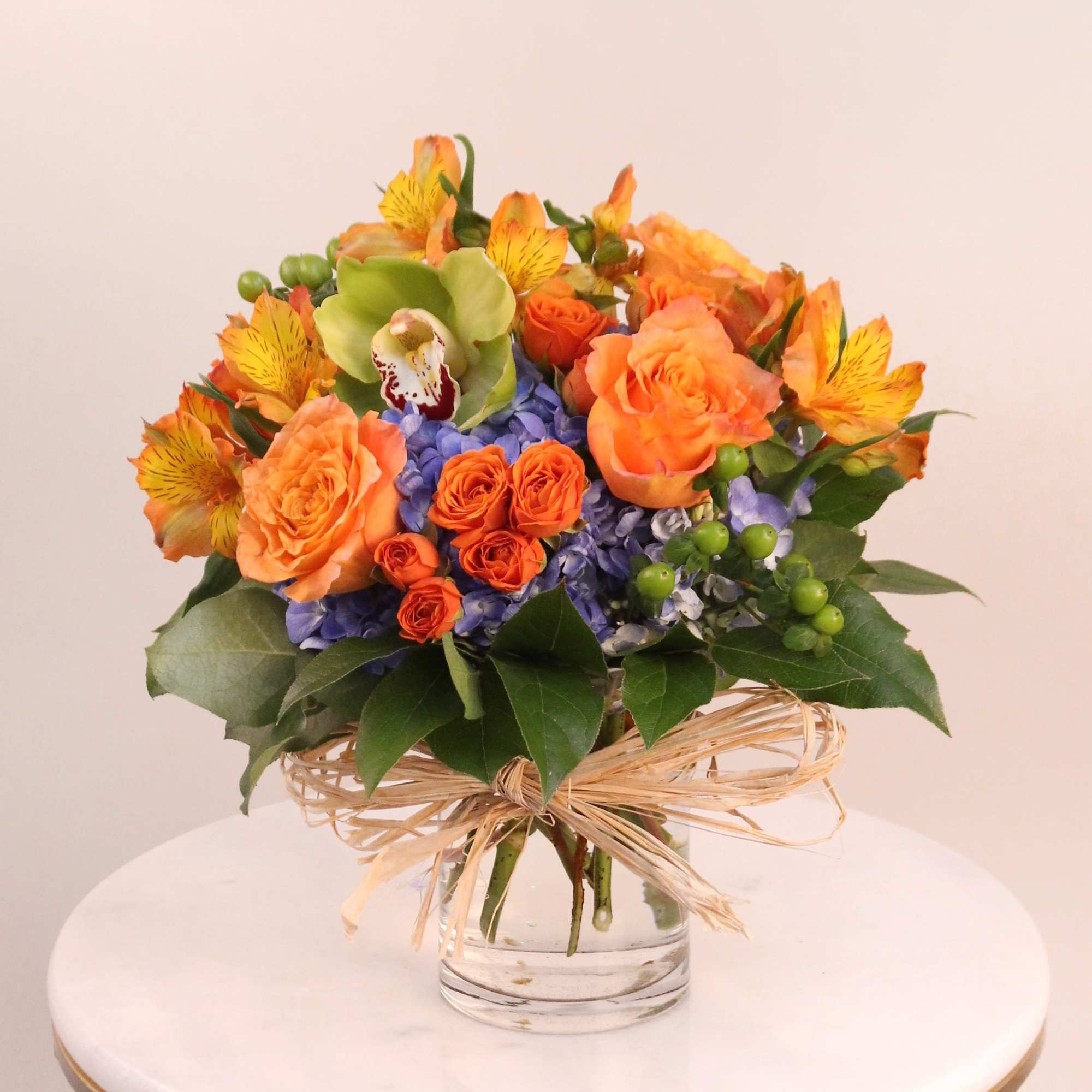 A bright and cheerful arrangement of hydrangeas, roses, orchid, alstromeria, and coffee