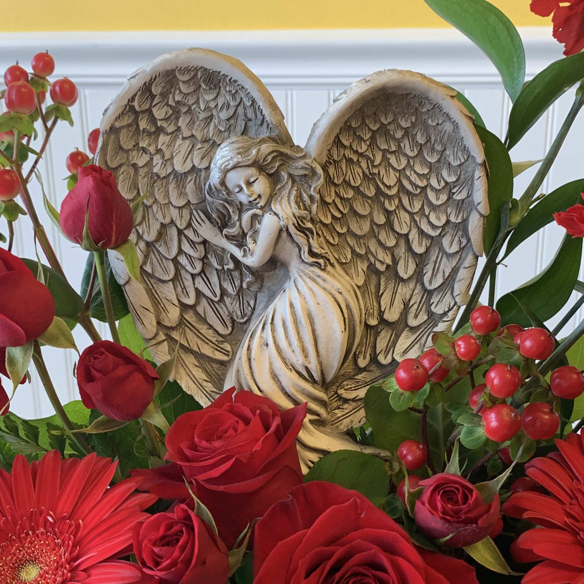 This peaceful angel sculpture, surrounded by radiant red flowers and delicate greenery