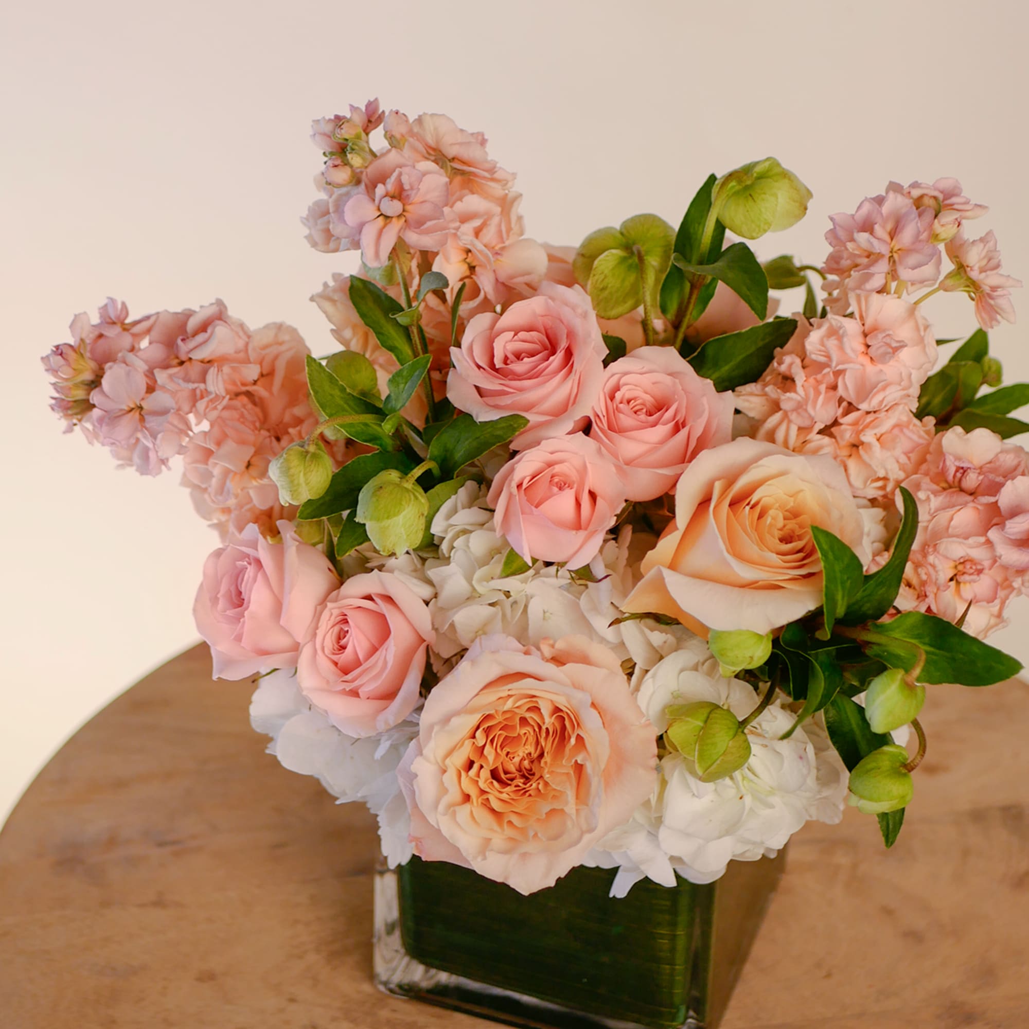 This bright arrangement boasts white hydrangeas, peach roses, fragrant peach stock, and