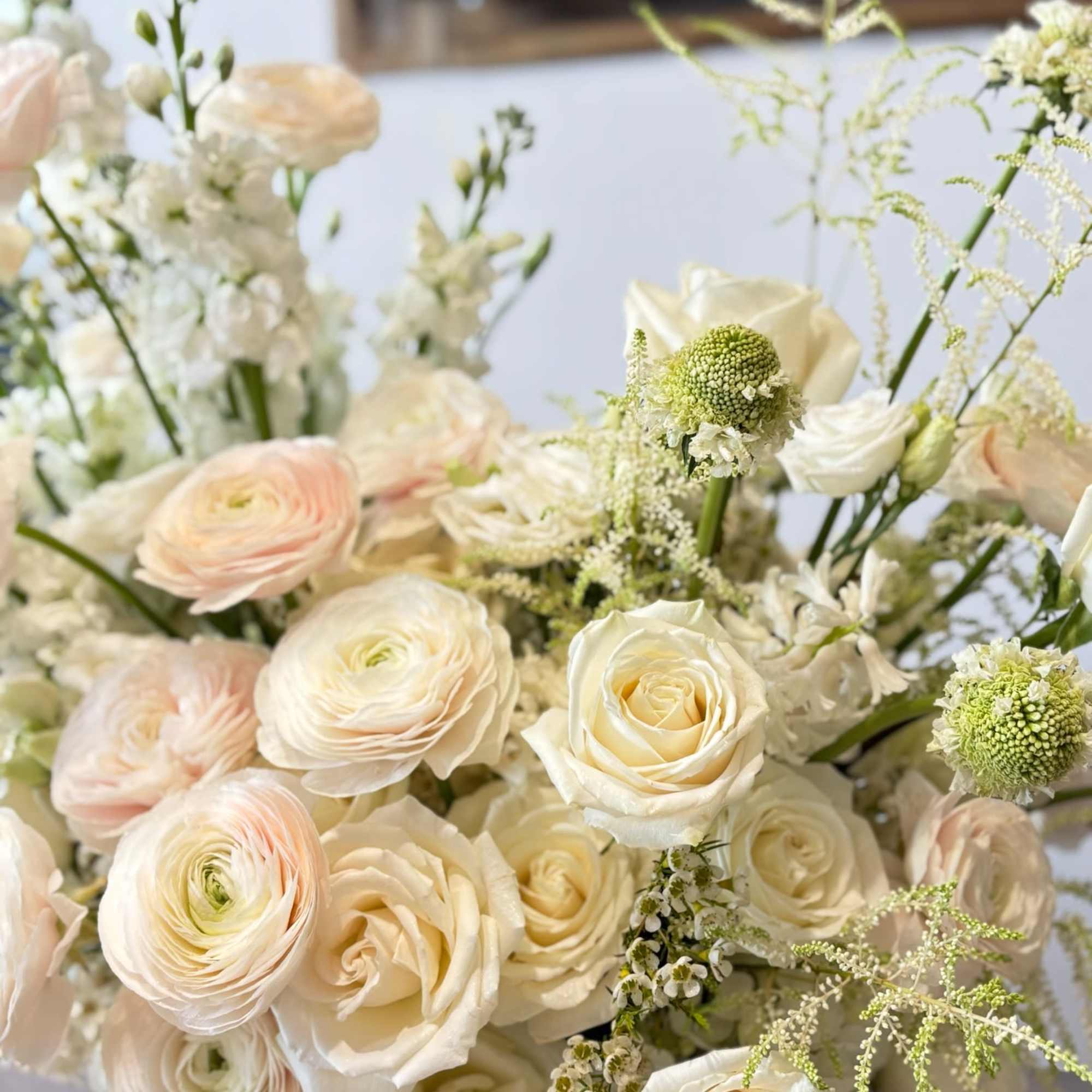 A grand and elegant arrangement featuring lush white and blush ranunculus, garden