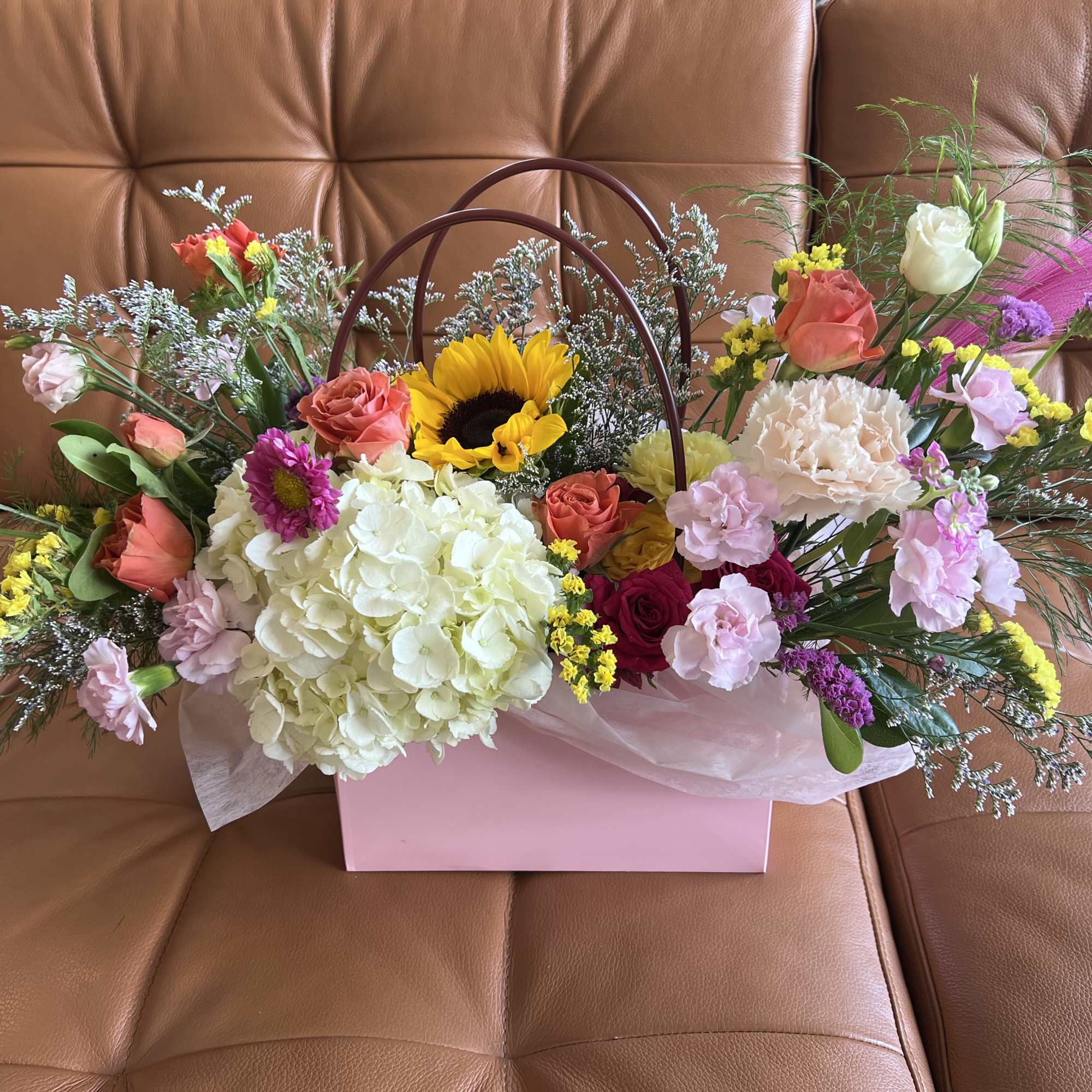 A charming gift bag overflowing with an array of seasonal blooms arranged