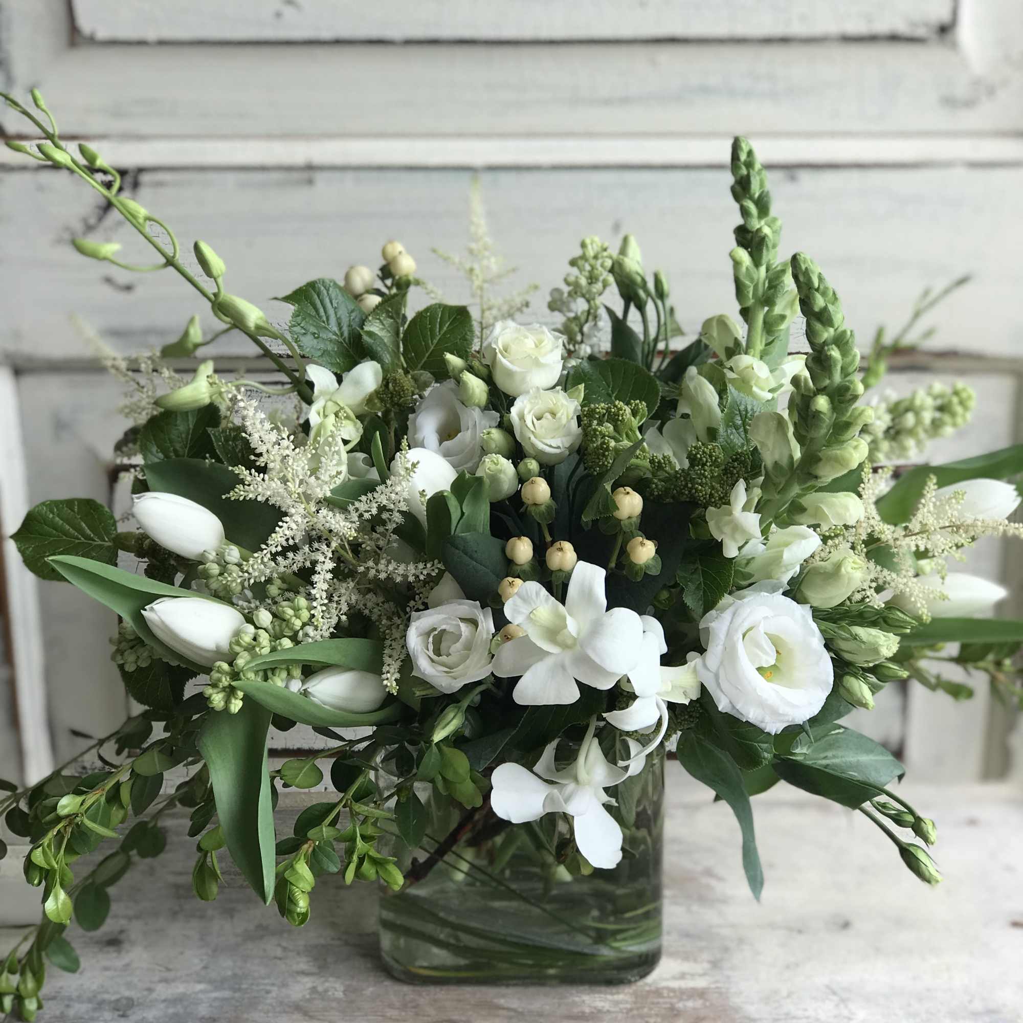 A mix of seasonal blooms in all white and unique foliage arranged
