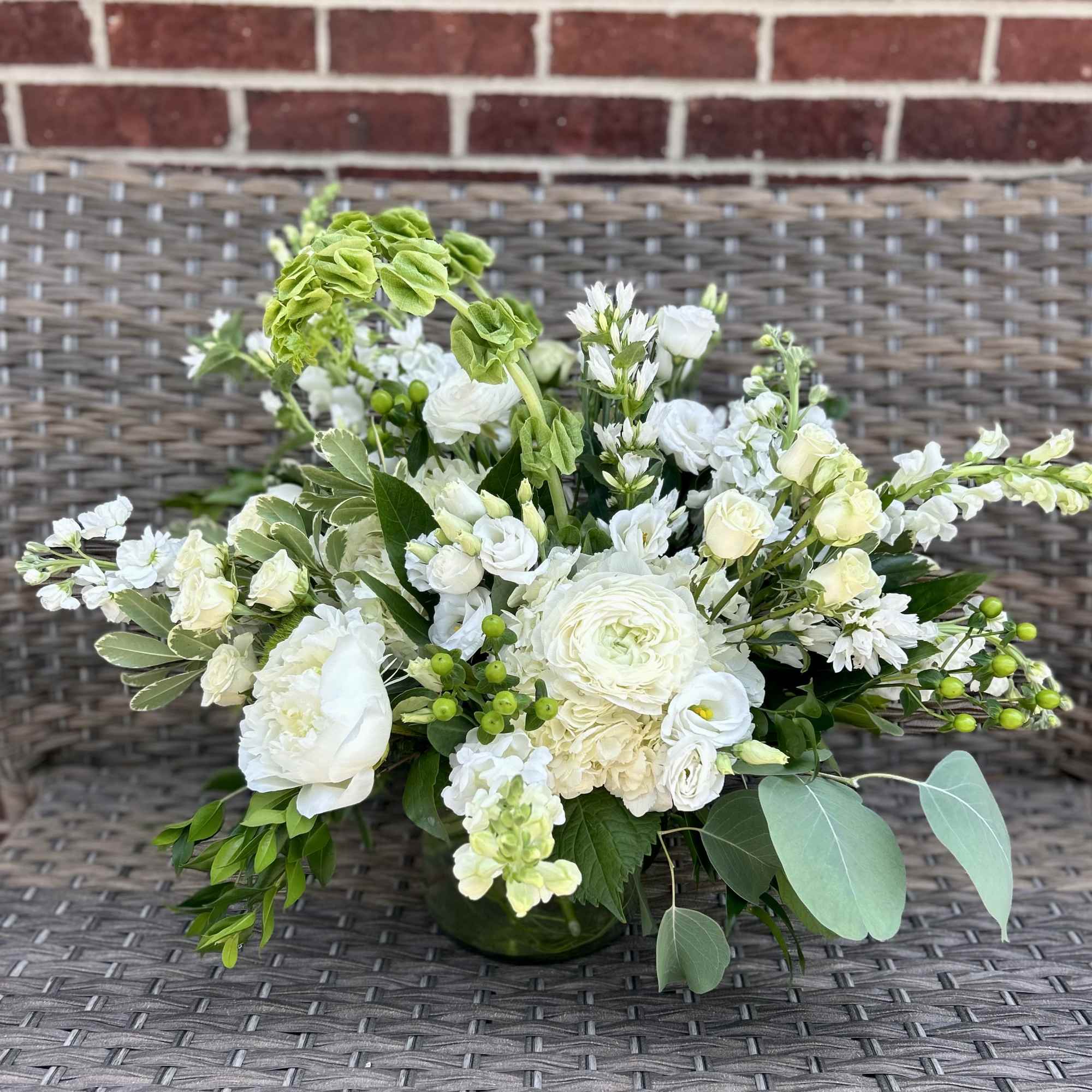 A mix of seasonal blooms in all white and unique foliage arranged