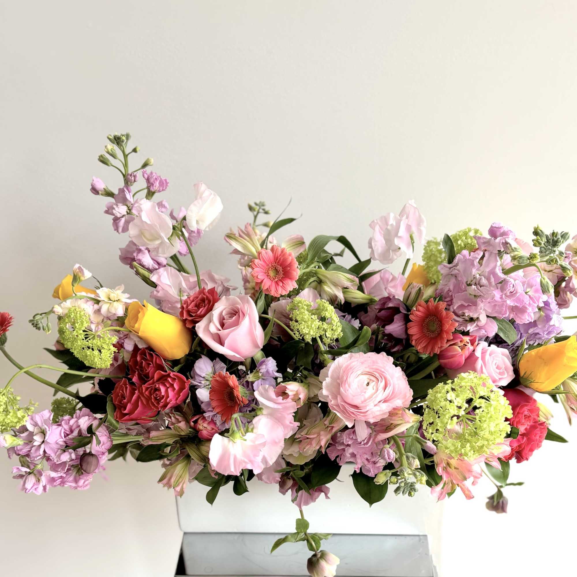 An elegant long flower centerpiece in a white ceramic rectangular container. A