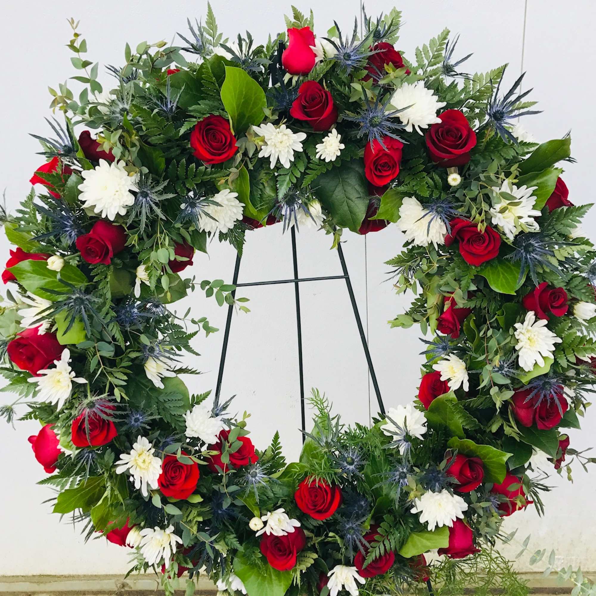 A large wreath filled with White Cushion Mums, Red Roses and Blue A large wreath filled with White Cushion Mums, Red Roses and Blue