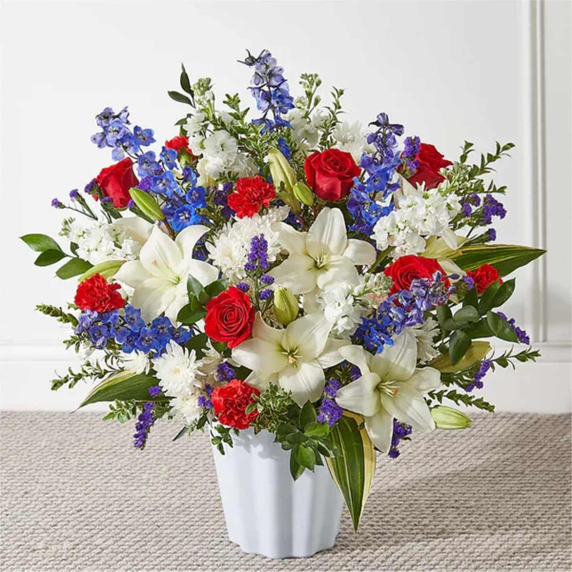 A collection of red roses, blooming white lilies, and blue delphinium come