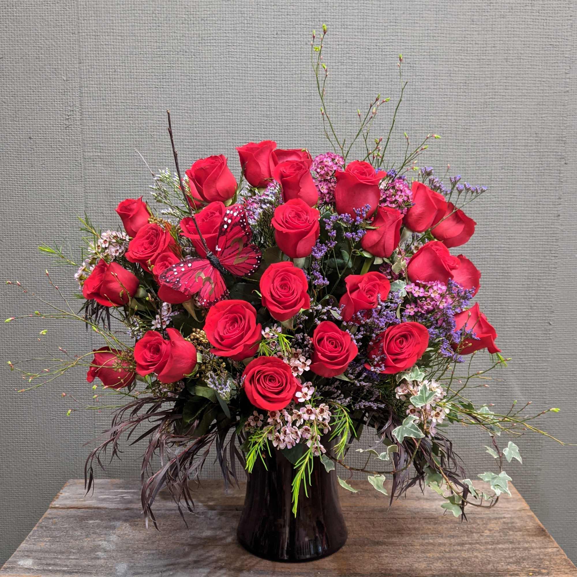 One dozen red roses with seasonal greens and filler in a vase. One dozen red roses with seasonal greens and filler in a vase.