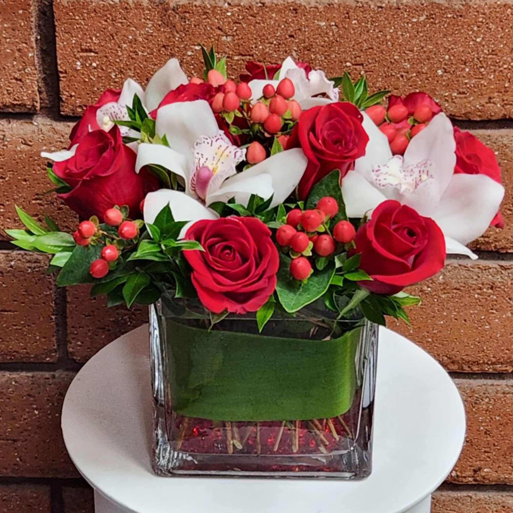 A striking fresh cut floral arrangement of premium red roses, white cymbidium