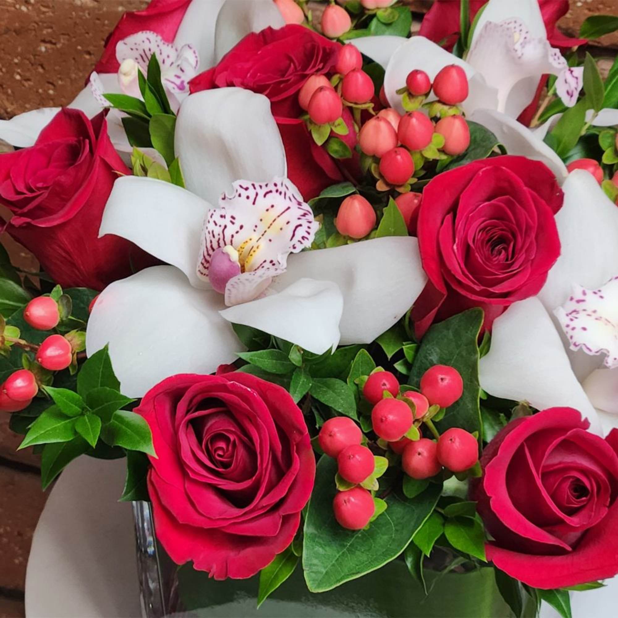 A striking fresh cut floral arrangement of premium red roses, white cymbidium