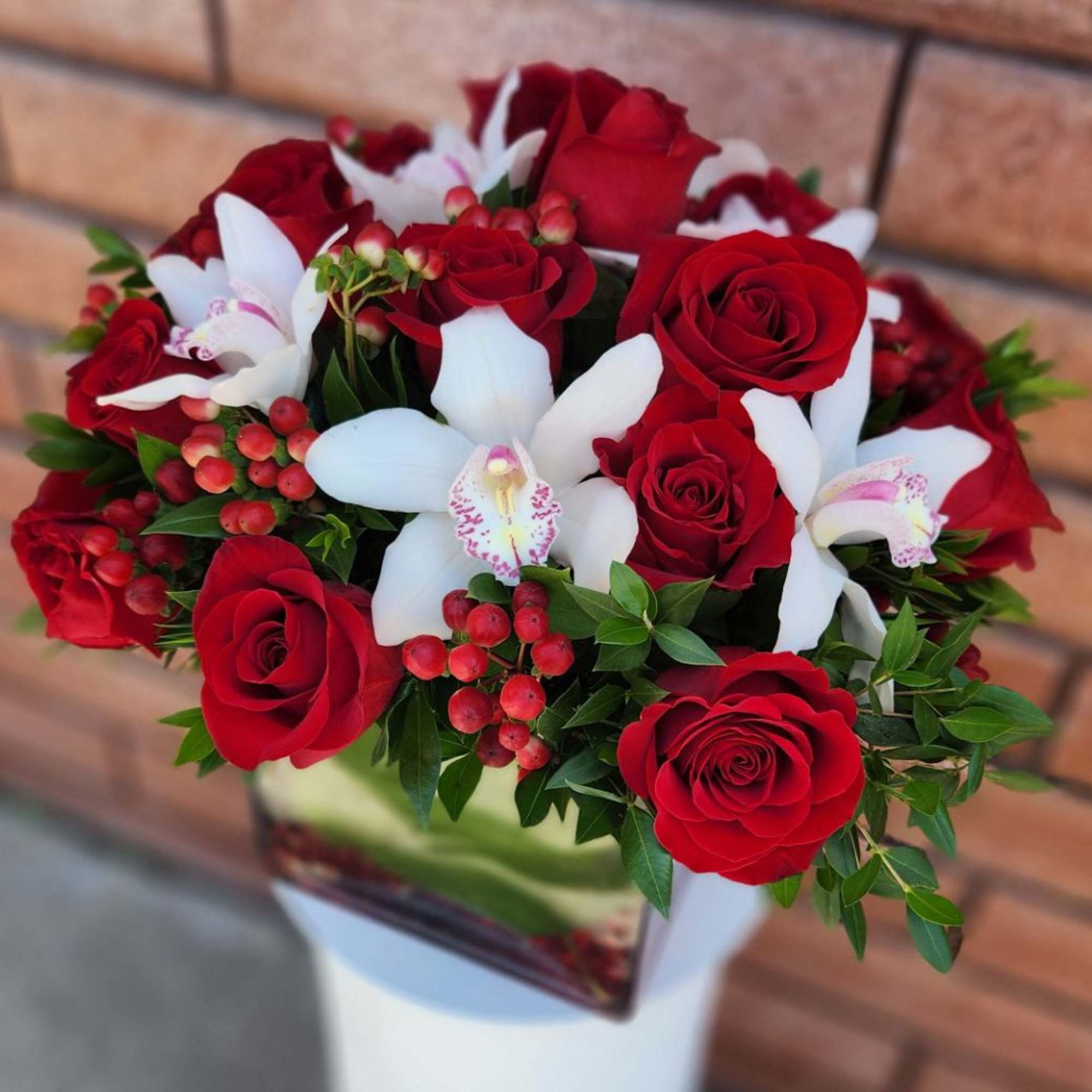 A striking fresh cut floral arrangement of premium red roses, white cymbidium