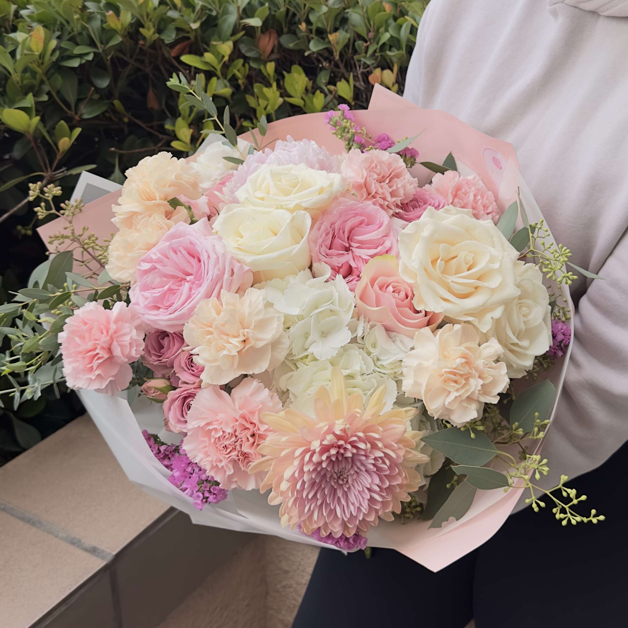 A round bouquet with white and pink flowers, wrapped in soft pink