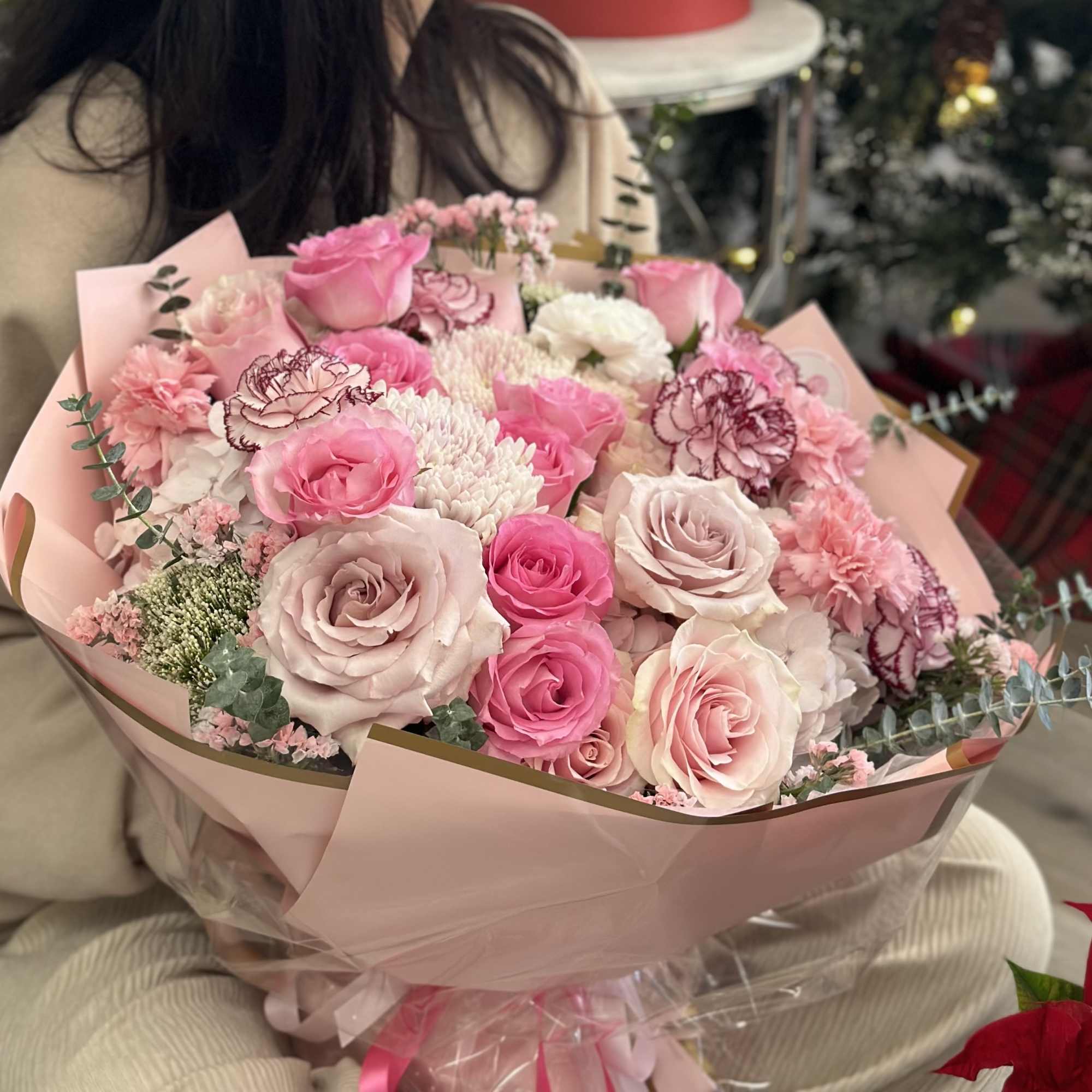 A round bouquet with white and pink flowers, wrapped in soft pink