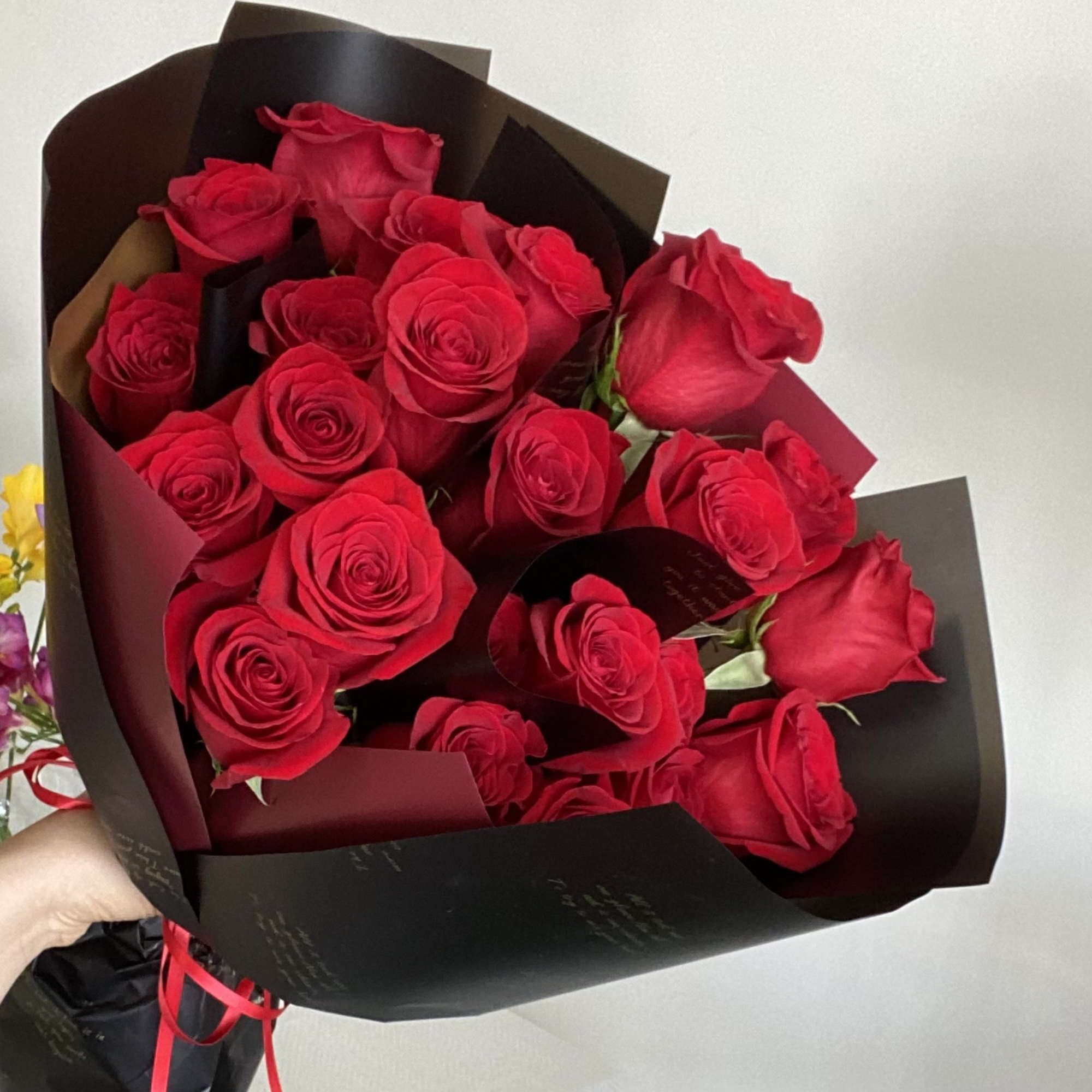 A front-facing bouquet of roses with layered paper accents, wrapped in black