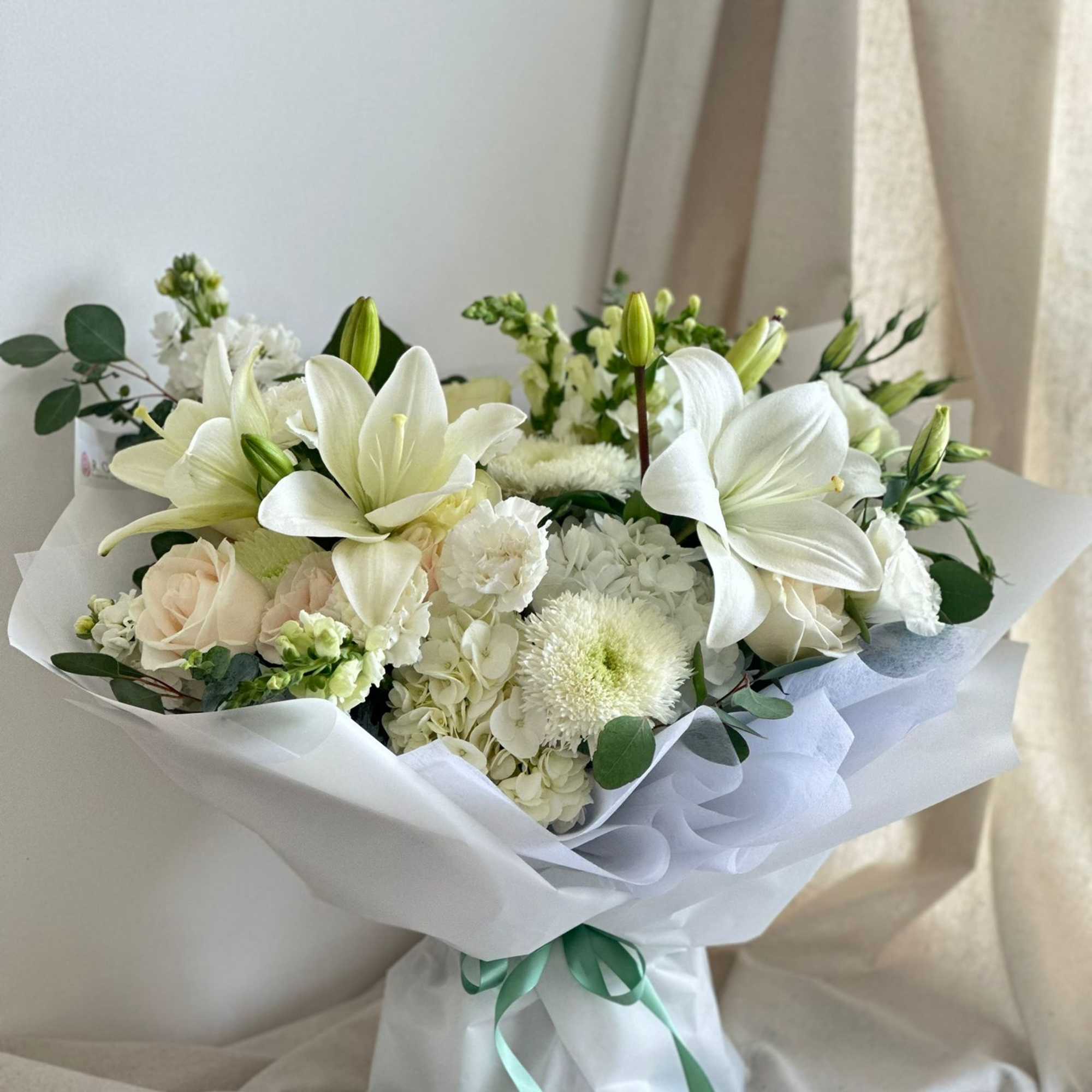 A front-facing bouquet with white flowers and greenery, wrapped in white paper.
