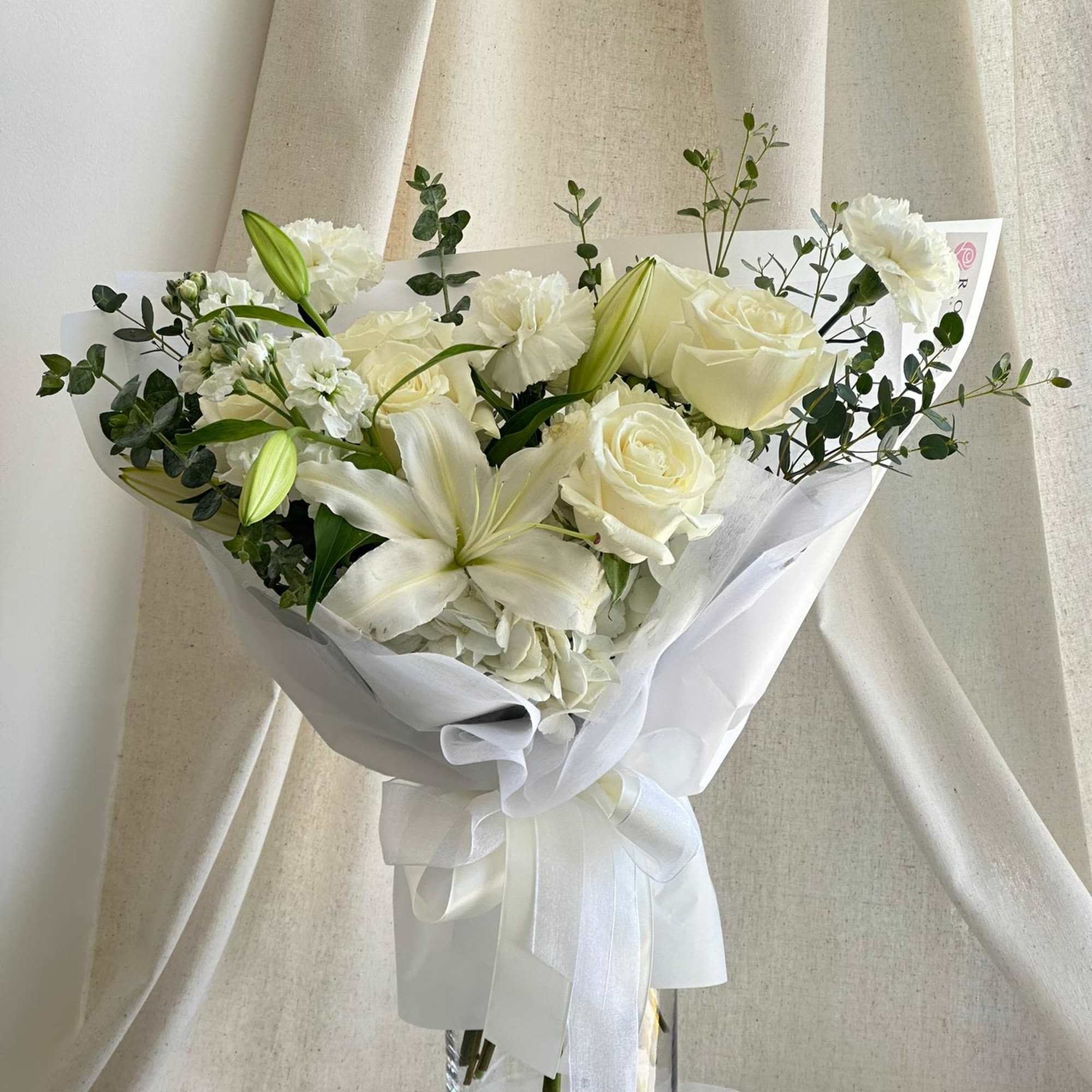 A front-facing bouquet with white flowers and greenery, wrapped in white paper.