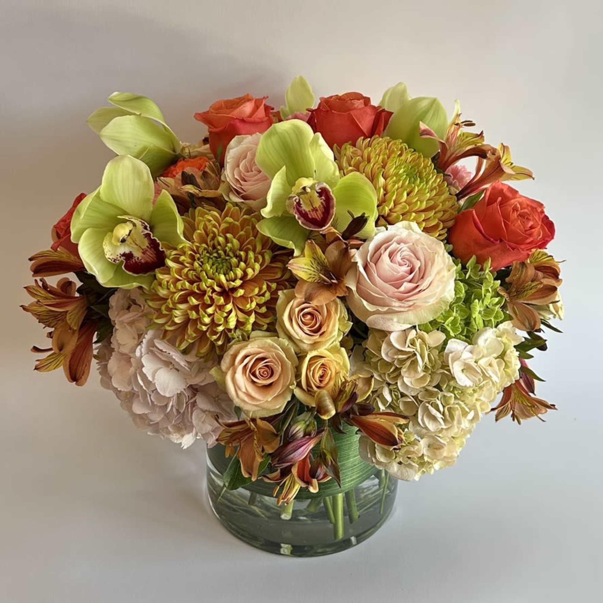 A compact arrangement with hydrangeas, orchids, protea, and a mixture of roses.