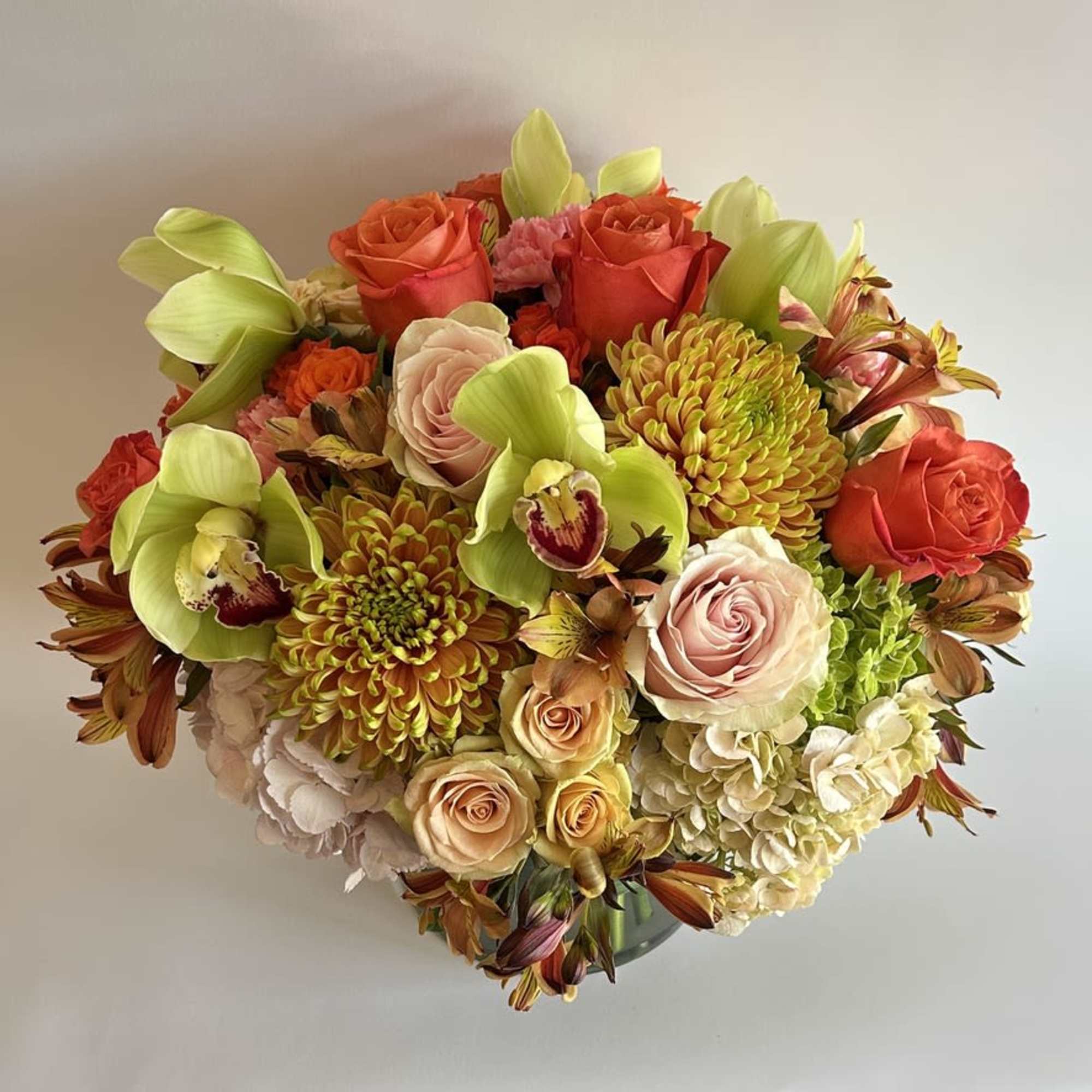 A compact arrangement with hydrangeas, orchids, protea, and a mixture of roses.