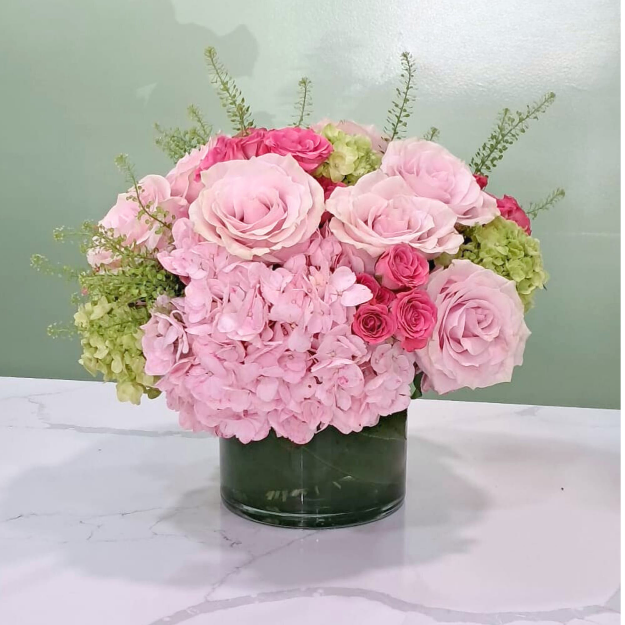 This sweet arrangement has pink and green hydrangeas, roses, spray roses, and