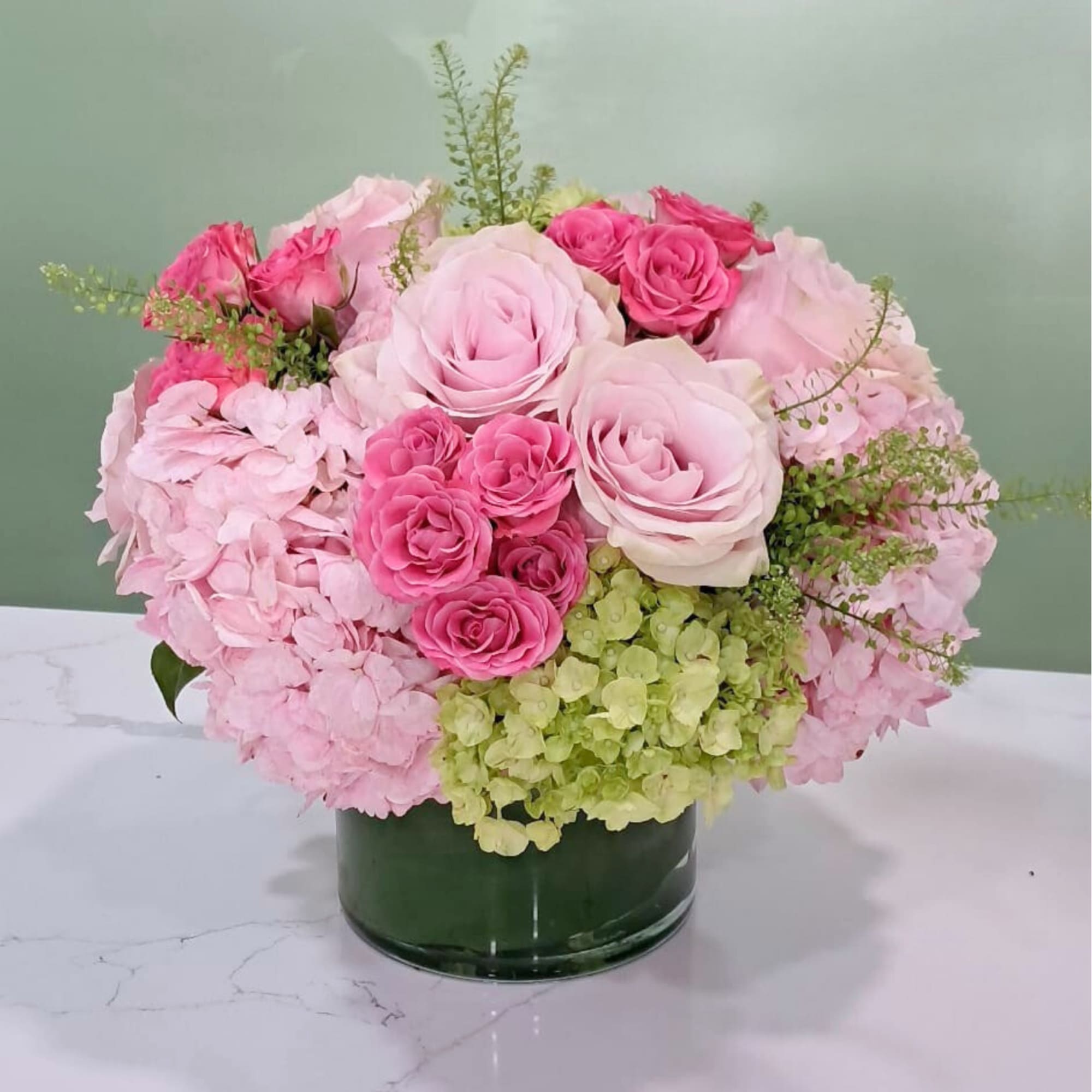This sweet arrangement has pink and green hydrangeas, roses, spray roses, and