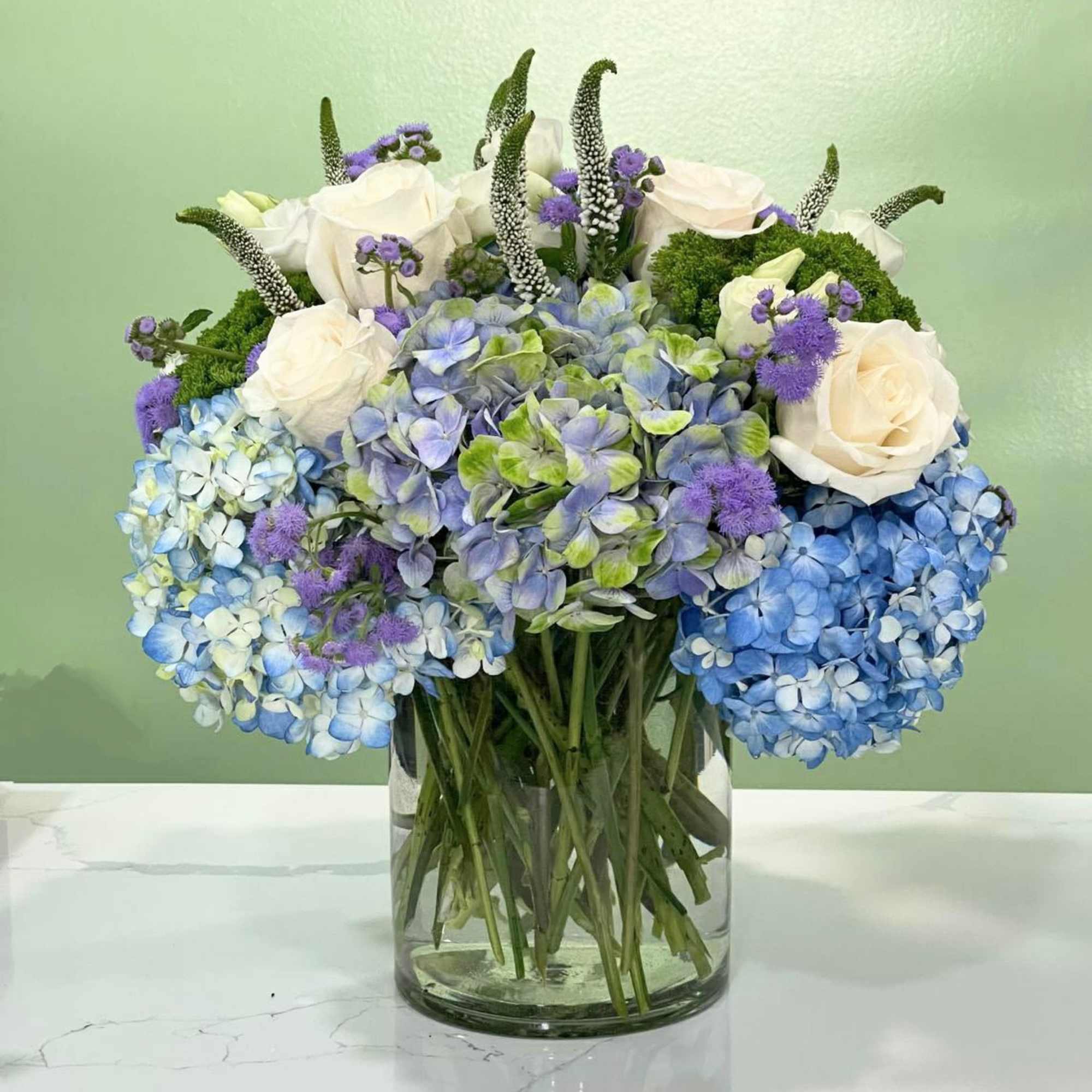 This gorgeous arrangement has blue and blue-green hydrangeas, Veronicas, roses, traceliums, floss
