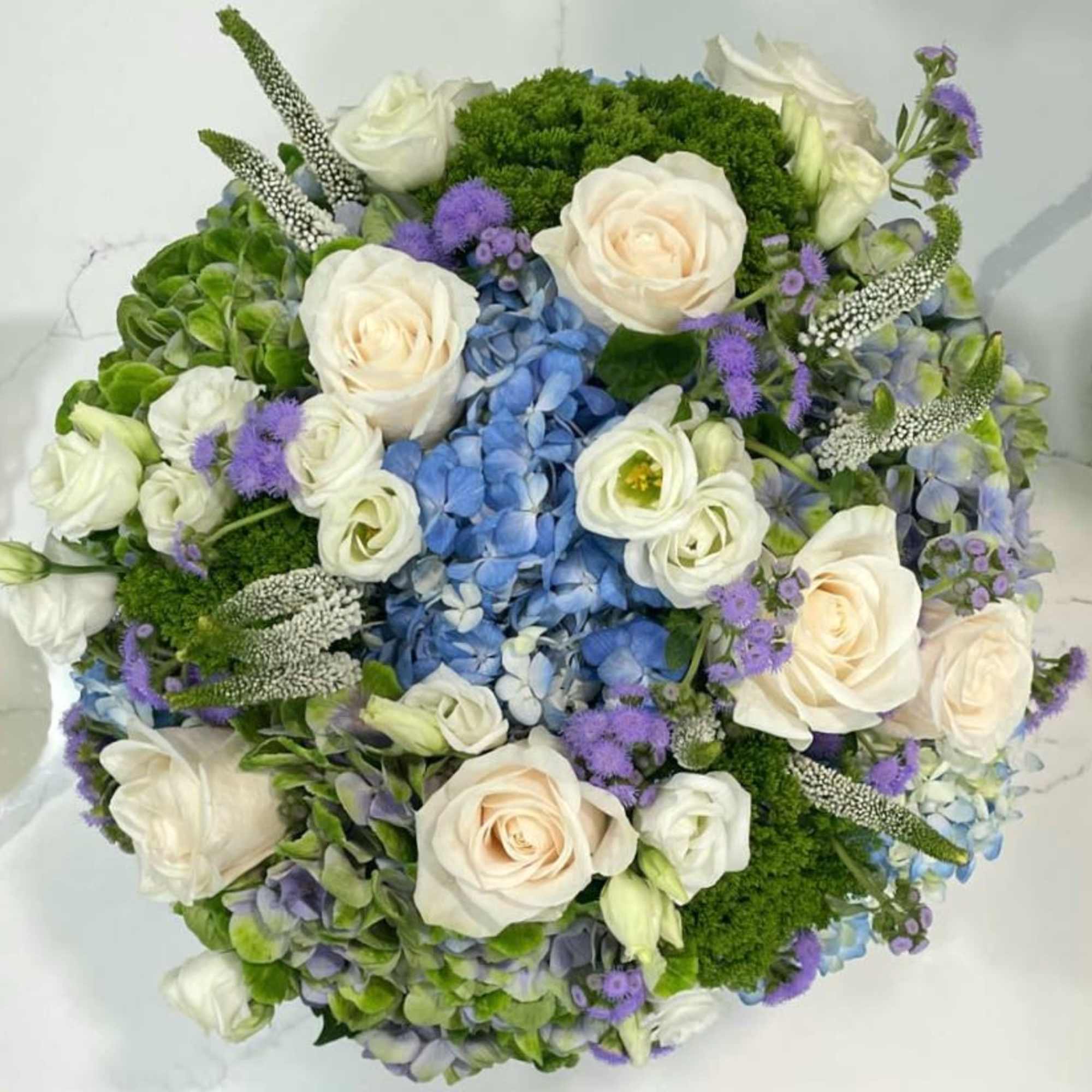This gorgeous arrangement has blue and blue-green hydrangeas, Veronicas, roses, traceliums, floss