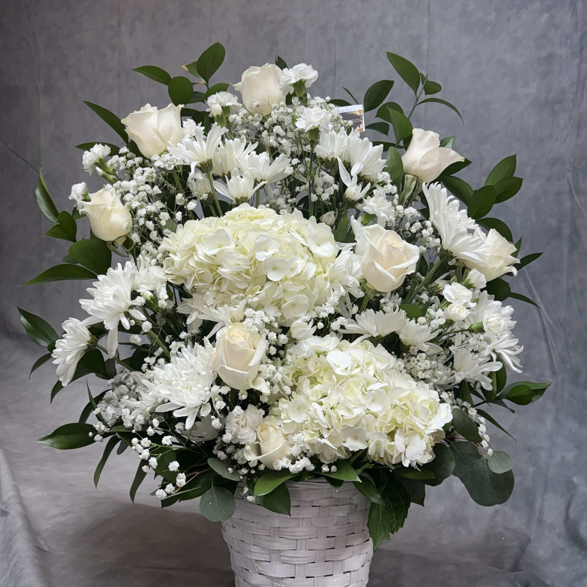 An elegant all-white display featuring lush hydrangeas, timeless roses, and soft  An elegant all-white display featuring lush hydrangeas, timeless roses, and soft