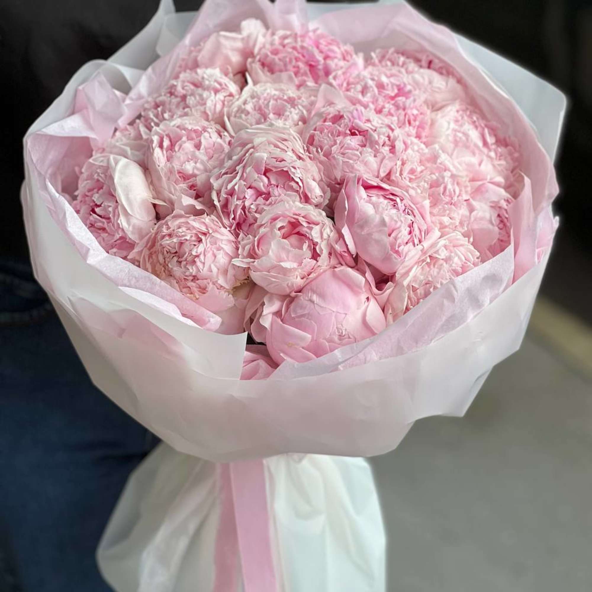A luxurious armful of lush, fully bloomed pink peonies, wrapped in layers
