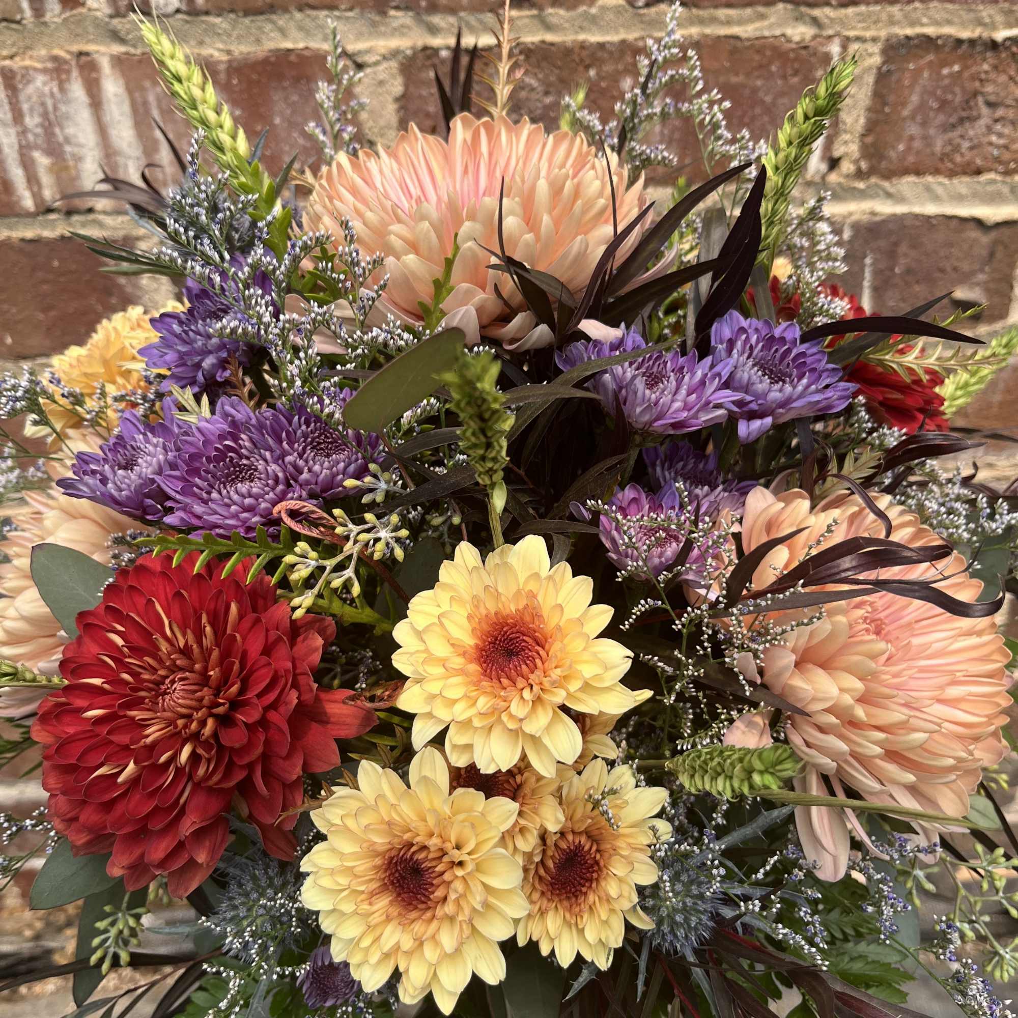 A variety of chrysanthemums with mixed greenery and accent flowers arranged in A variety of chrysanthemums with mixed greenery and accent flowers arranged in