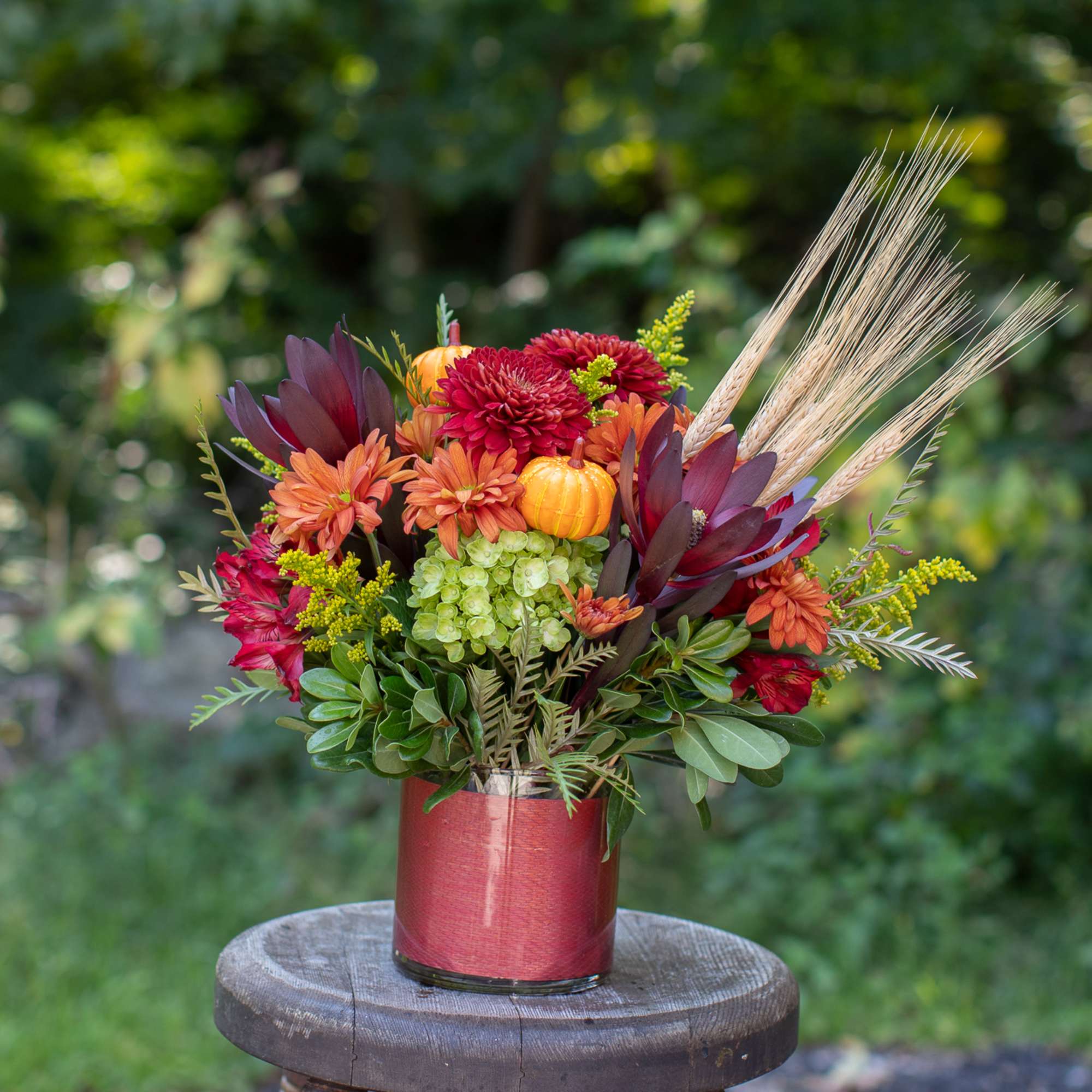 A cinnamon-gold cylinder vase adorned with festive pumpkins and natural dried wheat. A cinnamon-gold cylinder vase adorned with festive pumpkins and natural dried wheat.