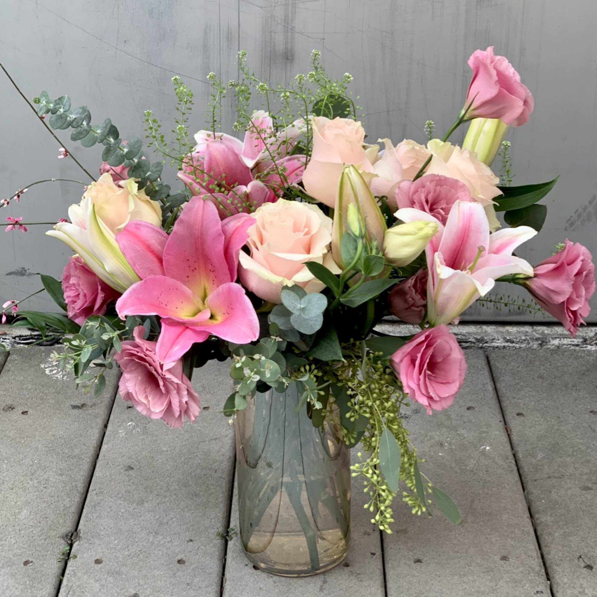 Pretty lilys, roses and ranunuculus in clear vase.
